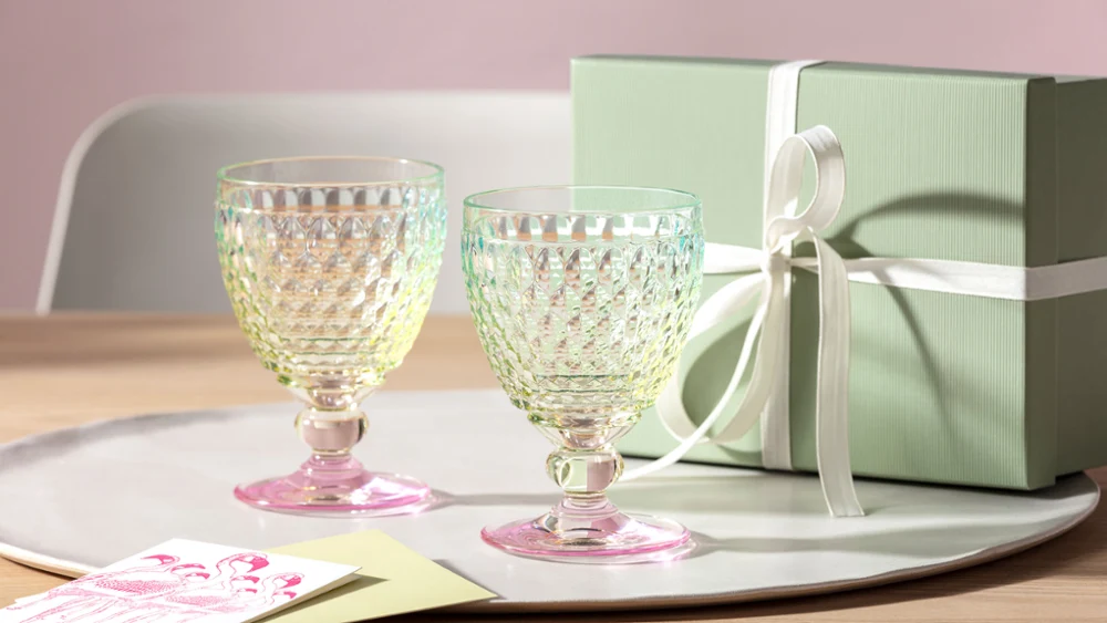 Twee Boston Pearl-glazen van Villeroy & Boch staan op een dienblad op een tafel naast een lichtgroene geschenkdoos, vastgebonden met een lint.