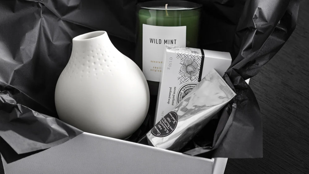 Een doosje met een kleine, witte Manufacture vaas van Villeroy & Boch met een crèmetube en een kaars in een glas. 