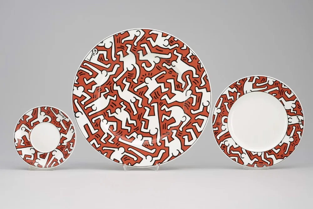 A tableware set includin three plates with red and white patterns and stylized human figures outlined in black.