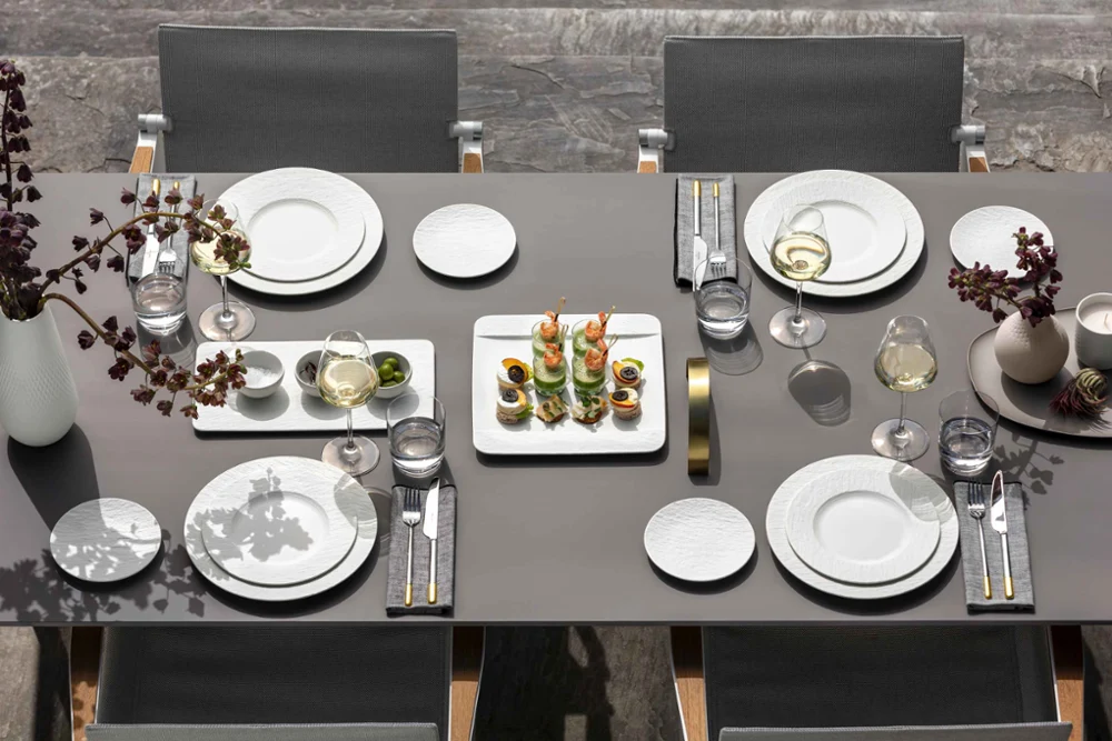 Manufacture Blanc Outdoor Dining Table Setting Modern outdoor dining table set with Manufacture Blanc porcelain dinnerware, La Divina wine glasses, appetizers, and gold-accented flatware for elegant al fresco entertaining.