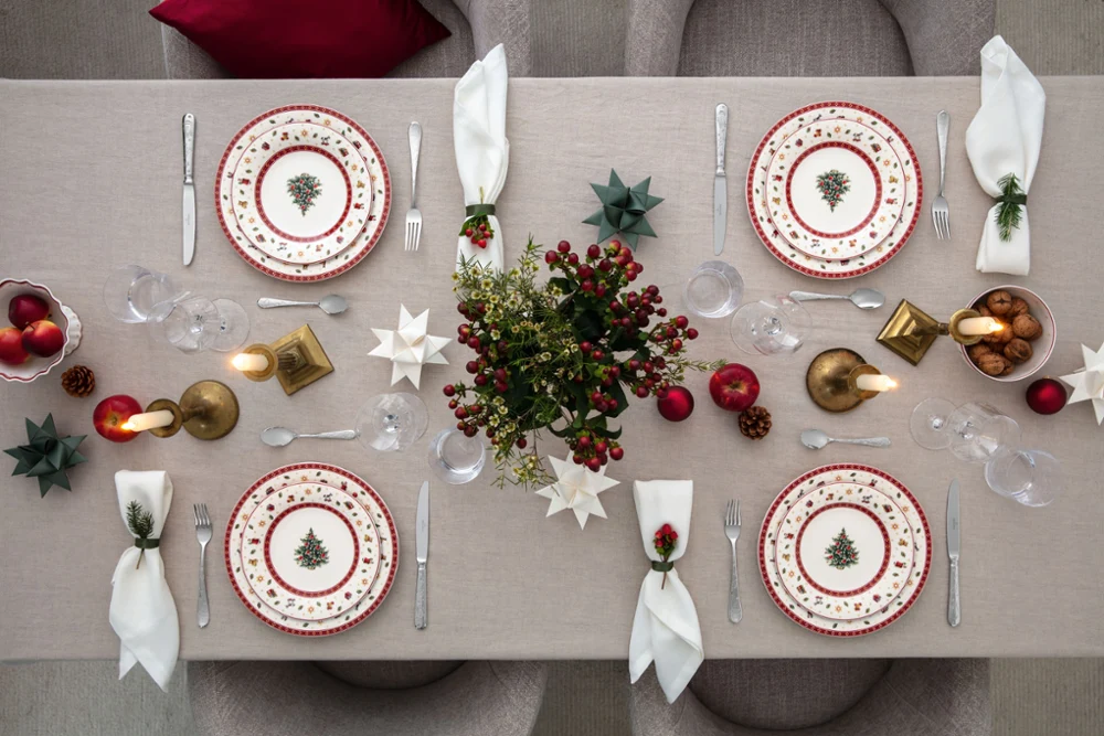 Top-down view of a Christmas-decorated dining table for four people with festive plates, candles, and decorative ornaments.