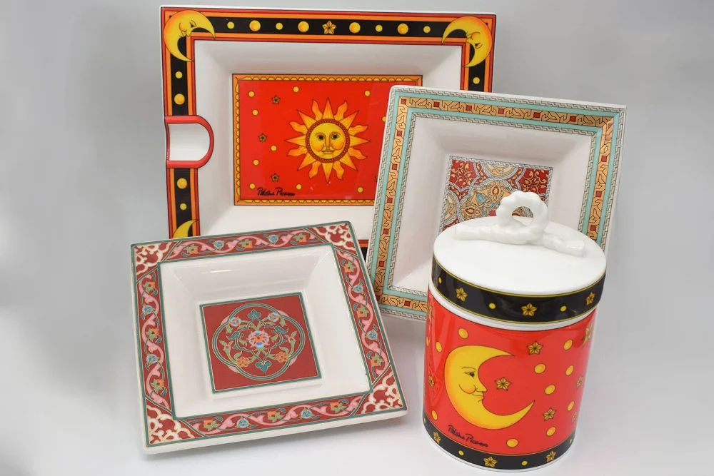 A tableware set including four ceramic plates and a bowl with sun, moon and star motifs in bright colors.