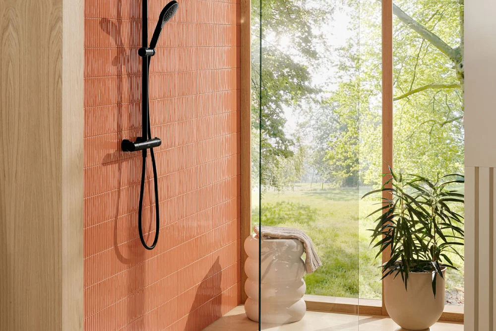 Verve Showers fitting with Architectura shower tray in a bright bathroom Modern shower with glass walls and black fittings next to a large window overlooking greenery.