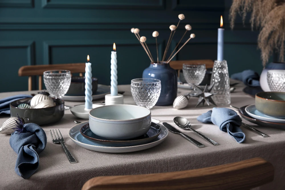 Dining table set for Christmas with Crafted plates and Boston glasses, in front of a blue-green paneled wall.