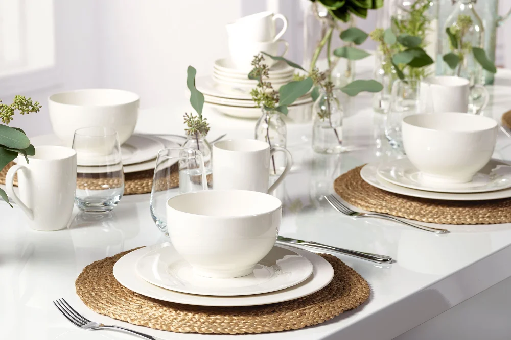 Elegant white dinnerware set from the Basic White collection by Villeroy & Boch on a table with decorative place settings and green plants.