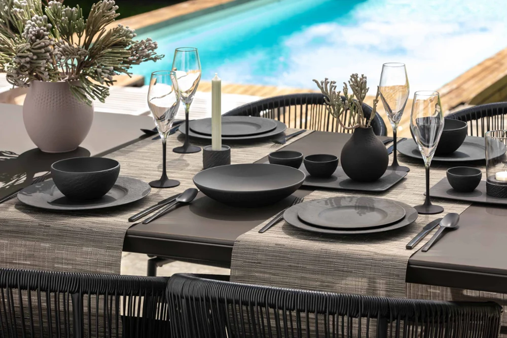 Black Manufacture dinnerware and glasses on a table by the pool Elegant outdoor dining area with black dinnerware and glasses from the Manufacture collection by a pool.