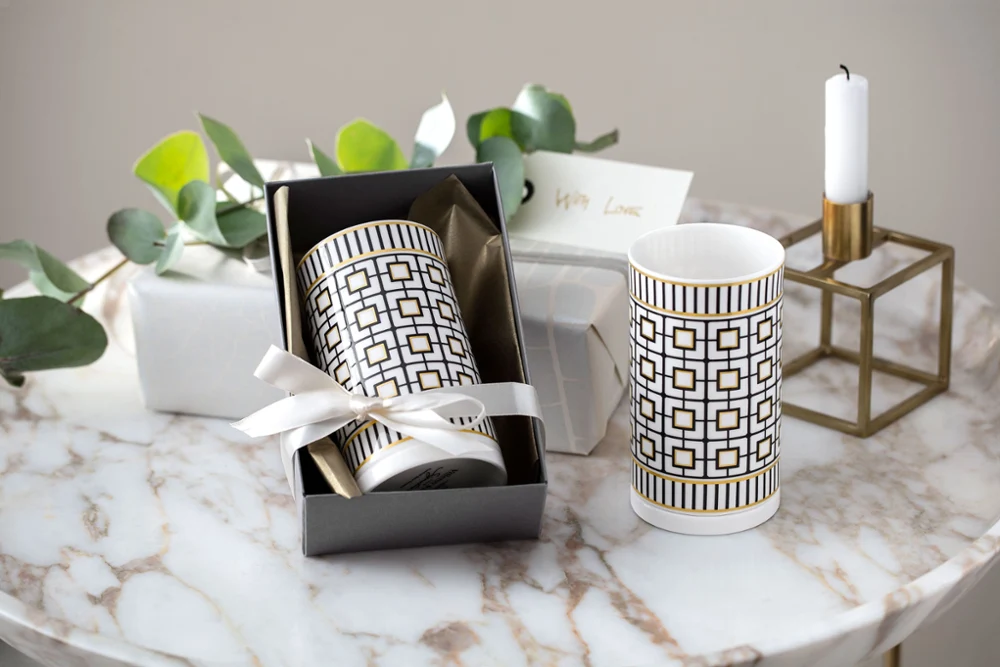 Two MetroChic vases in a gift box, accompanied by candles and a card on a marble table.