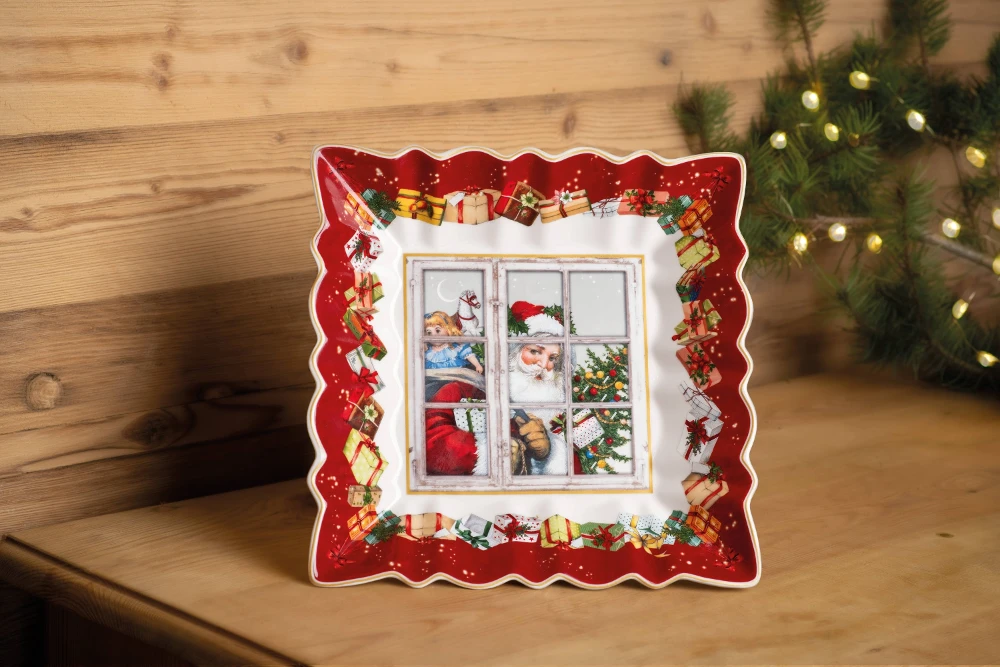 Toy's Fantasy Square Santa Plate Square Christmas plate with a scalloped red border, decorated with gift illustrations. The center depicts a cozy scene with Santa, a child, and a dog by a window. The setting is warm and festive.