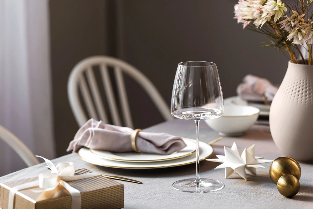 A table set for Christmas with an Anmut Gold wine glass and MetroChic dinnerware with gold decorations.
