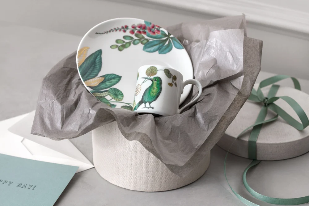 A Villeroy & Boch Avarua plate and cup in front of a gift box, presented with an envelope and box lid.