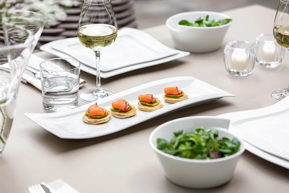 A table set for a meal with plates of appetizers, glasses of white wine, a bowl of salad, and tea lights.