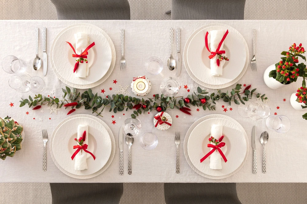 Festive dining table setting for Christmas with Manufacture plates, red ribbons, and Christmas decorations.
