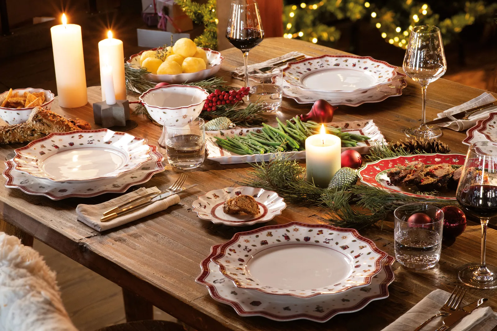 A festive dining table setting with patterned plates, glasses, and flatware from Villeroy & Boch Toy’s Delight, while the lighted candles and Christmas decorations complete the ambience.