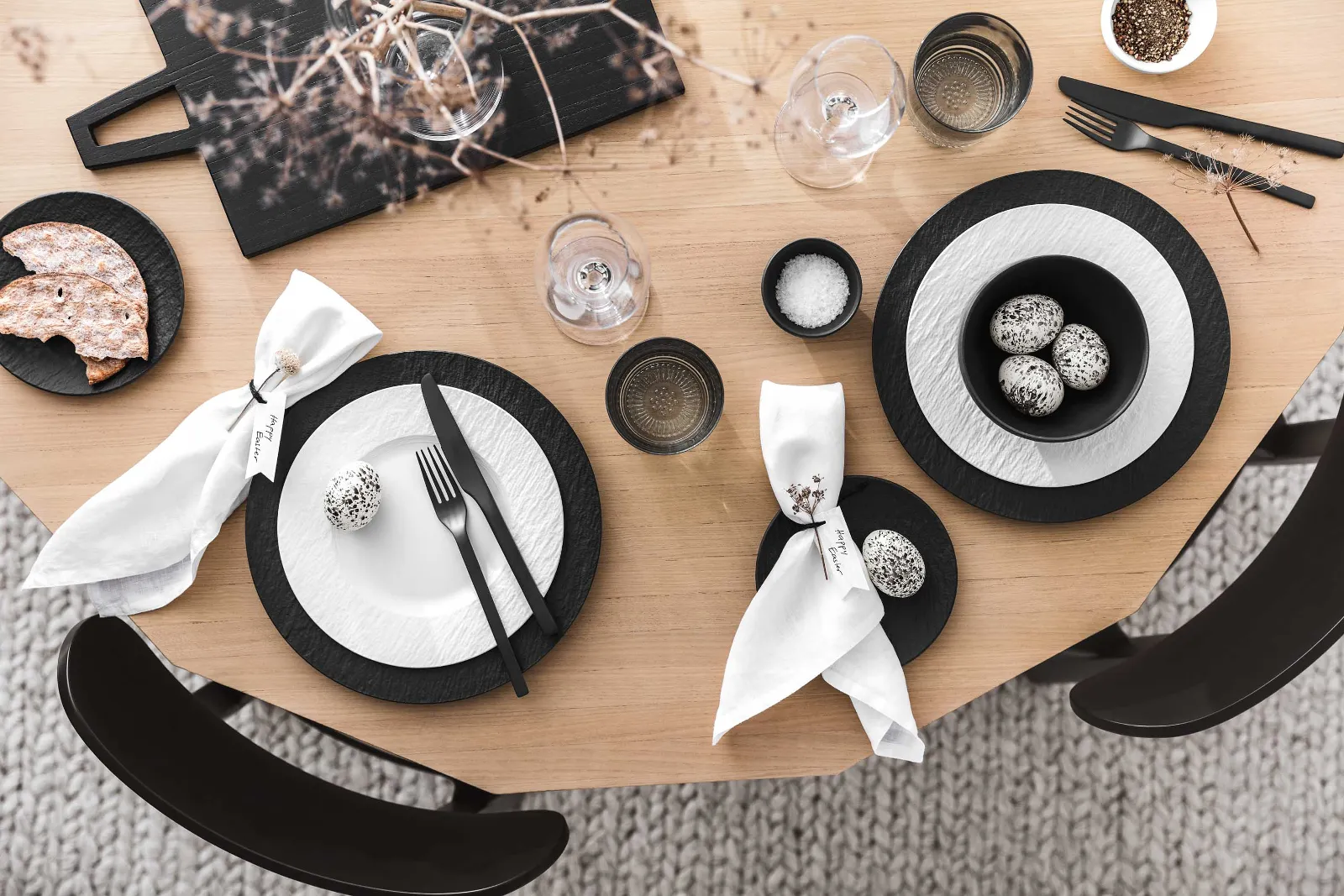 A modern dining table with black and white crockery and cutlery from the Manufacture collection and minimalist Easter decorations.