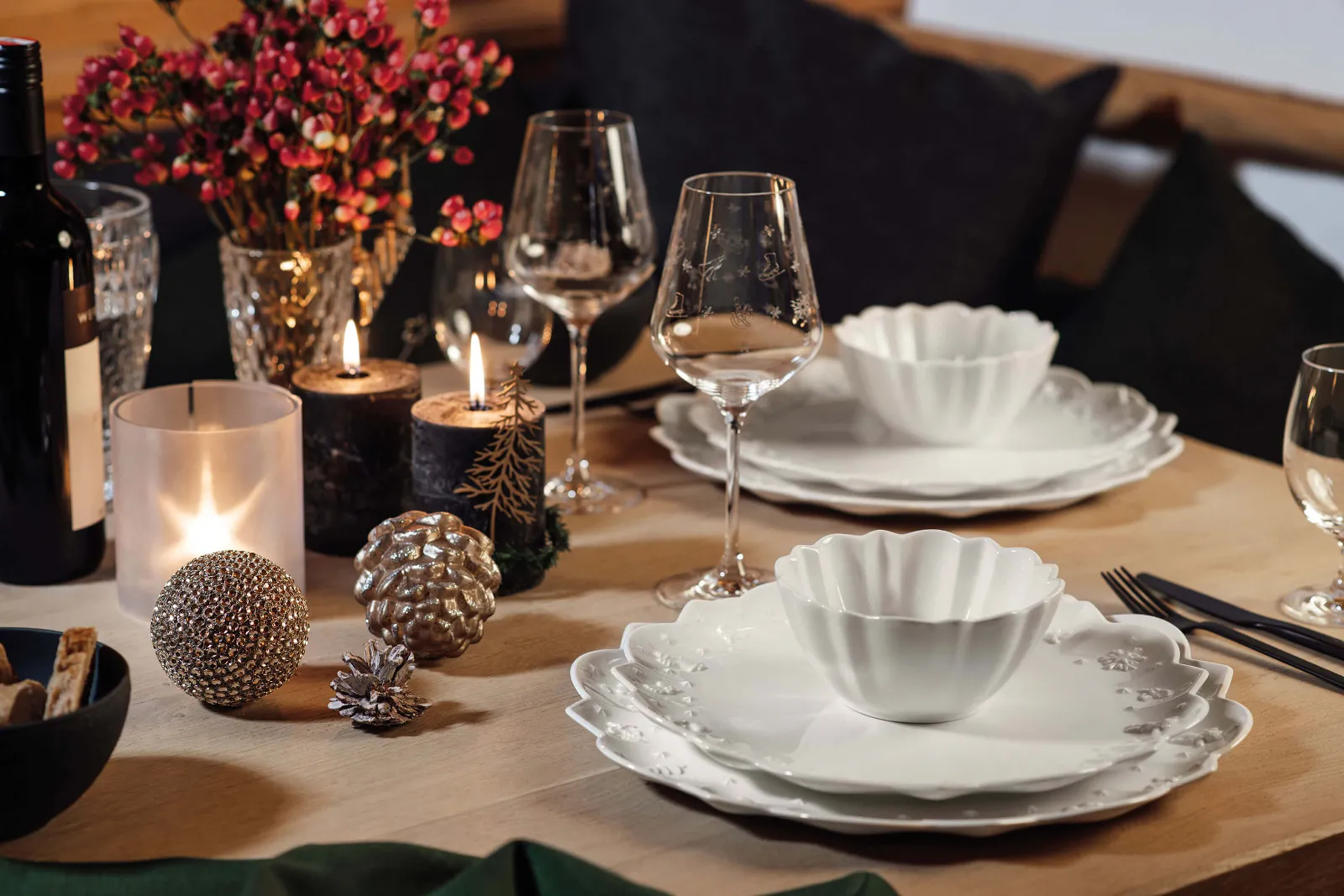 A dining table with white Toy’s Delight Royal Classic plates, wine glasses, candles, and decorative ornaments. Flowers and a bottle of red wine are also on the table.