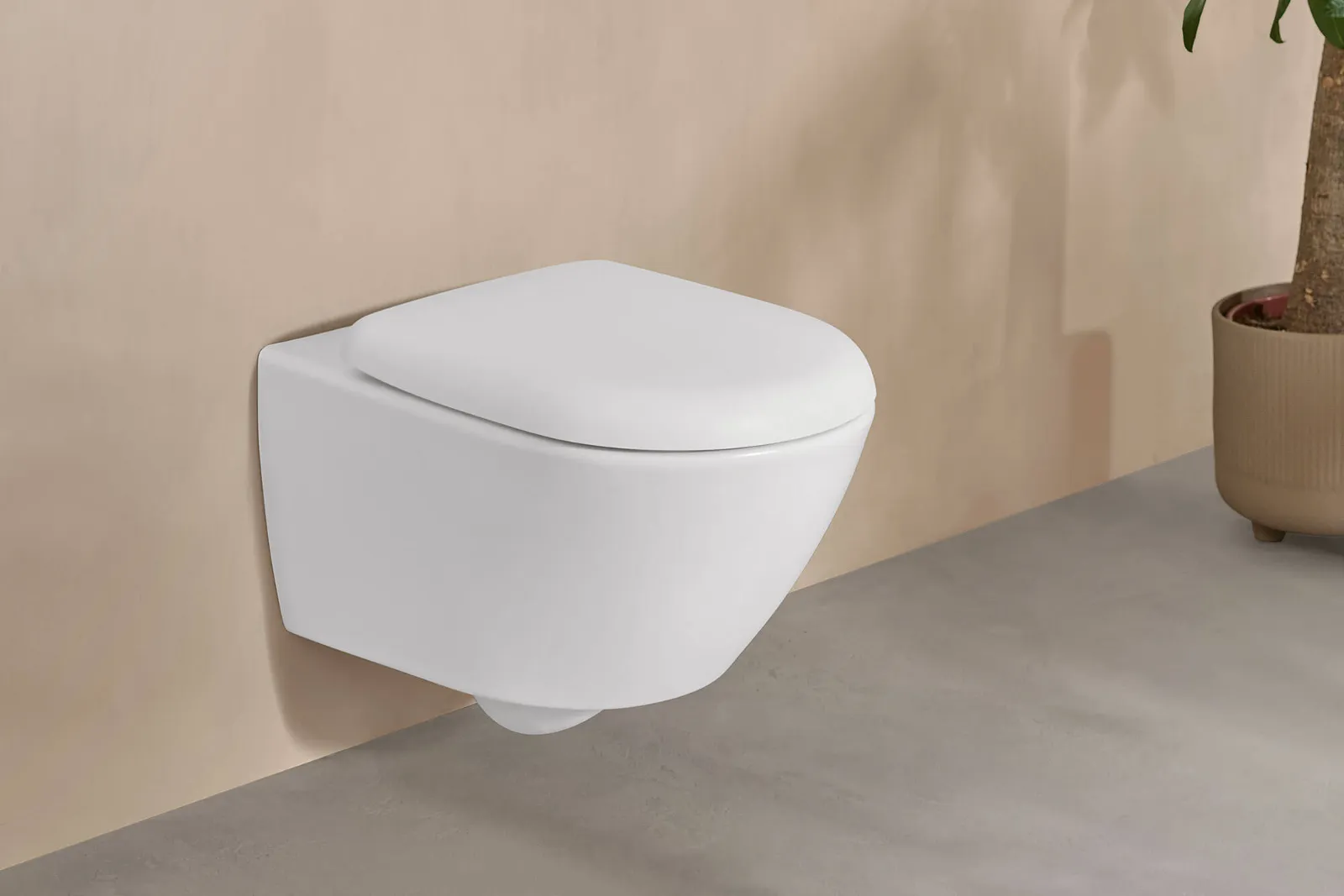 Et hvitt Antao-toalett fra Villeroy & Boch i et elegant beige baderom med en potteplante.