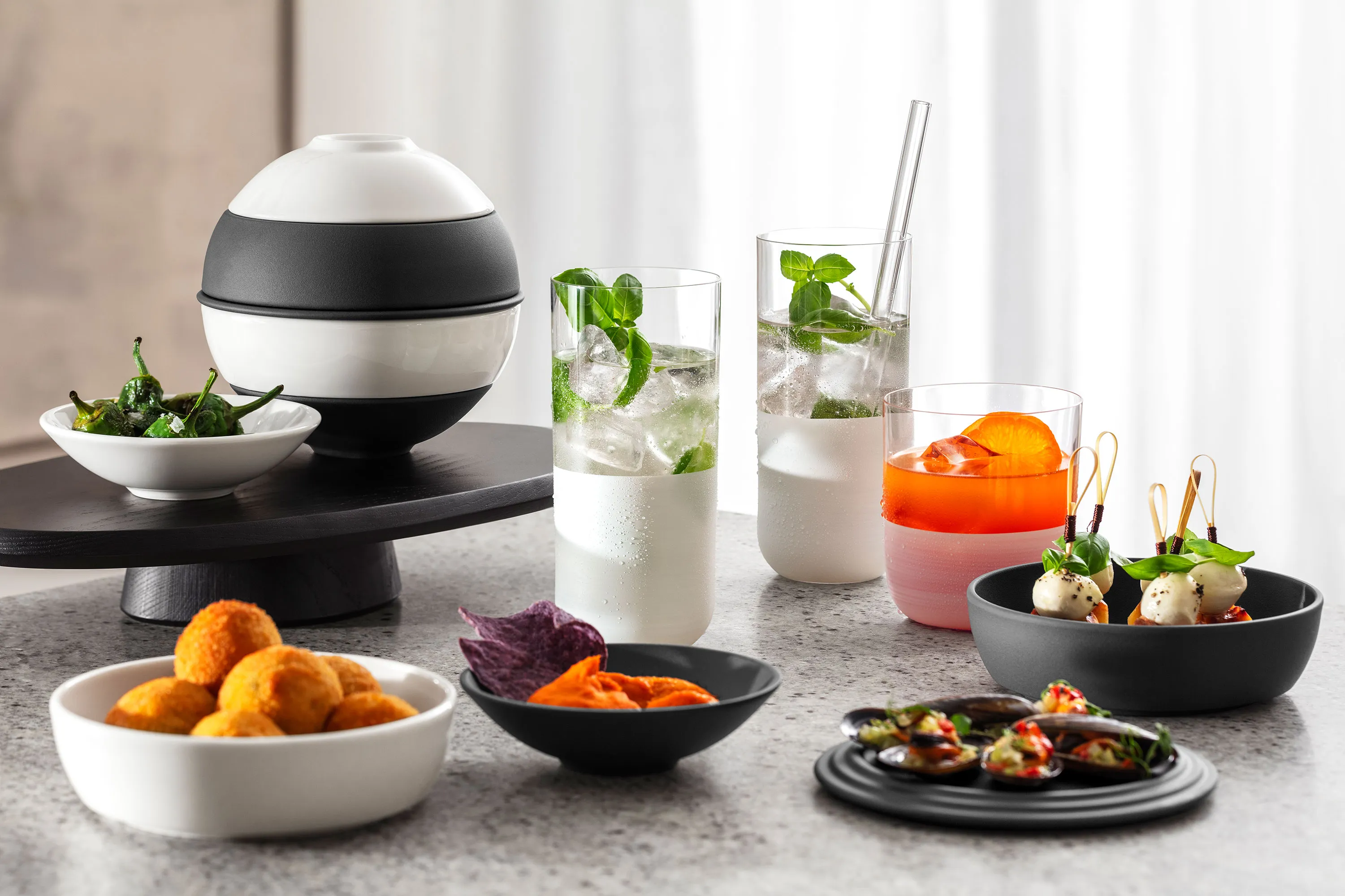La petite Boule noir et blanc présentée sur un plan de travail en marbre La petite Boule noir et blanc présente sur un plan de travail en marbre différentes entrées, dont des amuse-gueules frits, des chips violettes, des brochettes et des boissons avec garnitures.