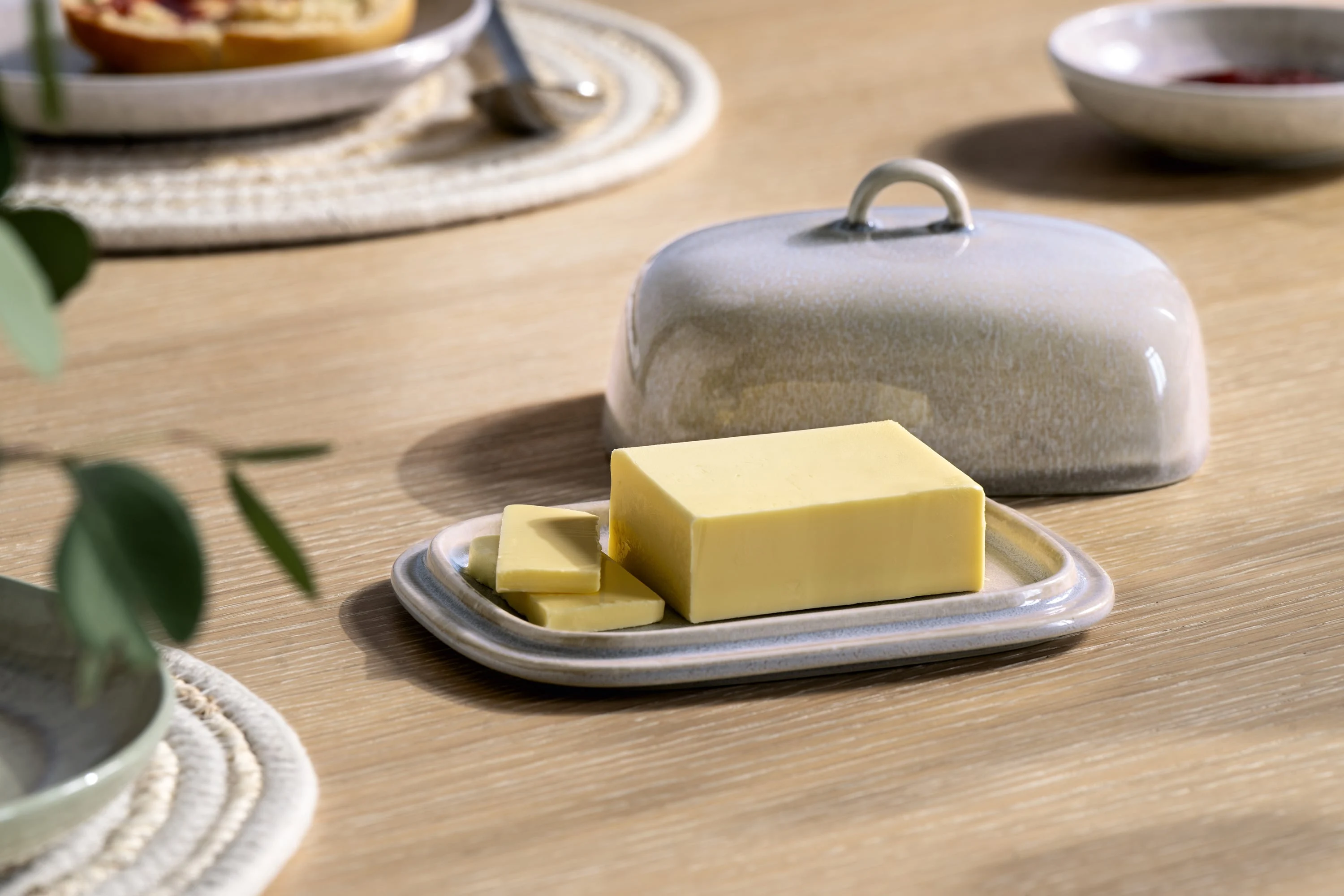 Un bloc de beurre rectangulaire avec deux tranches repose sur un beurrier en céramique Perlemor avec couvercle assorti sur une table en bois.