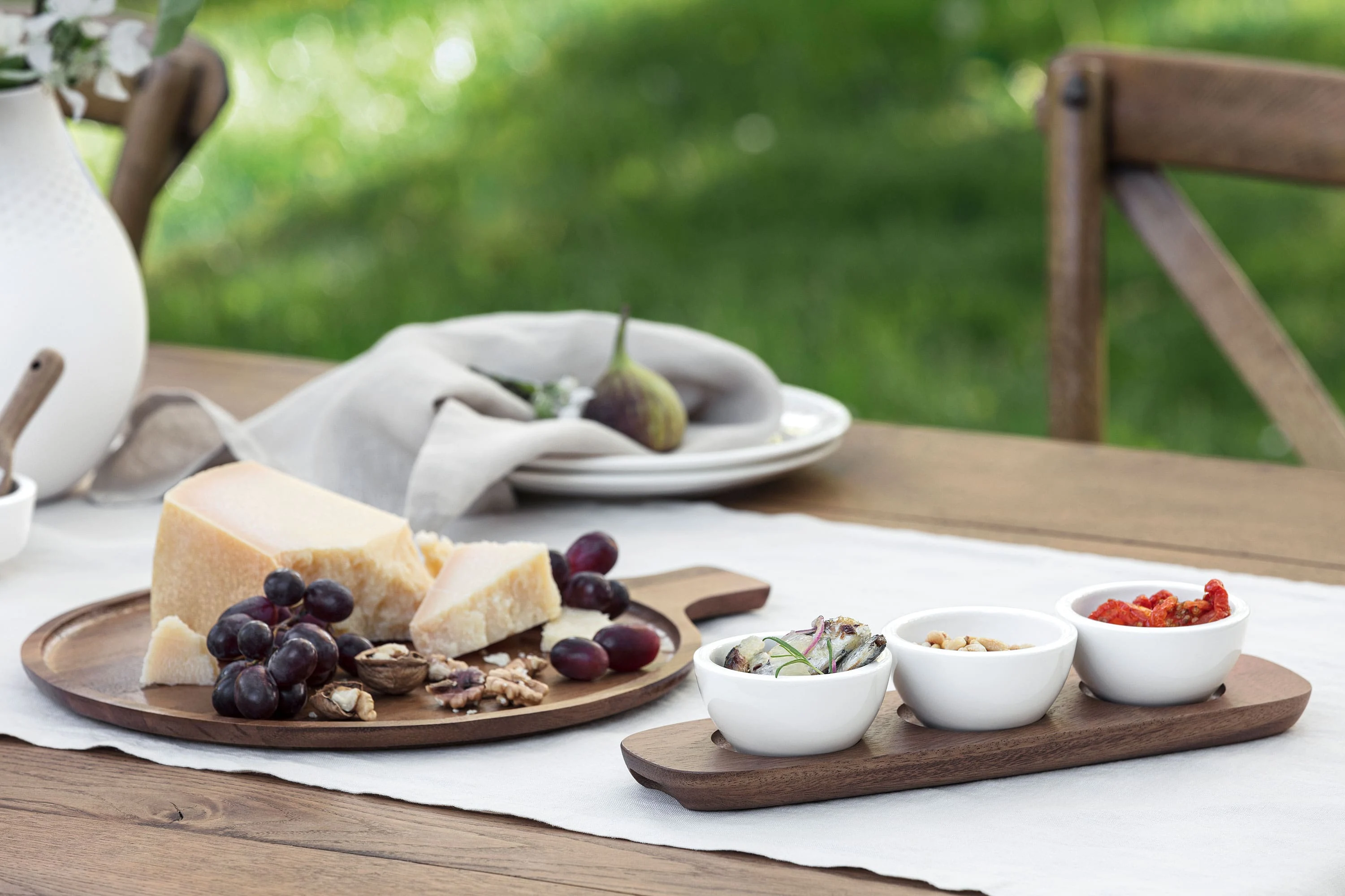 Villeroy & Boch Artesano wooden board, decorated with cheese, grapes, walnuts and figs. They are accompanied by three small dip bowls containing sliced vegetables, nuts and sun-dried tomatoes.
