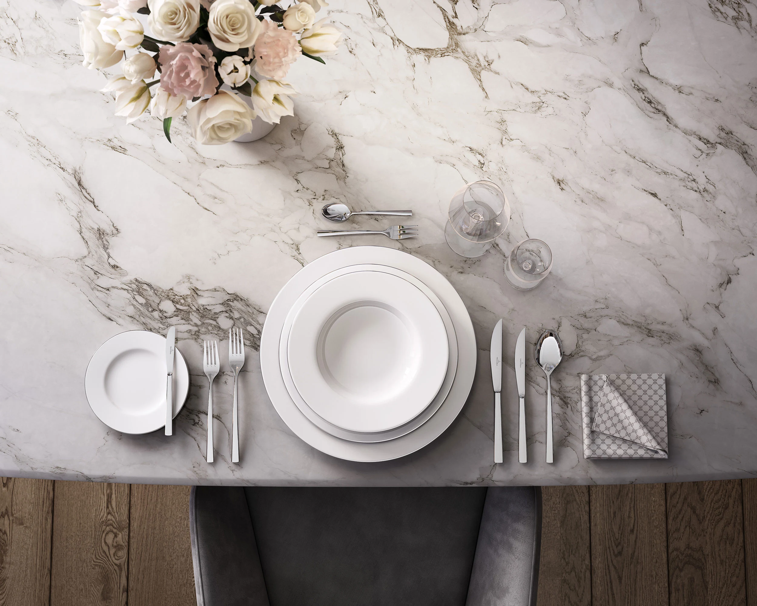Eine elegante Tischdekoration mit weißem Anmut Geschirr, Piemont Besteck, Gläsern und einem Blumengesteck auf einer Marmorplatte.