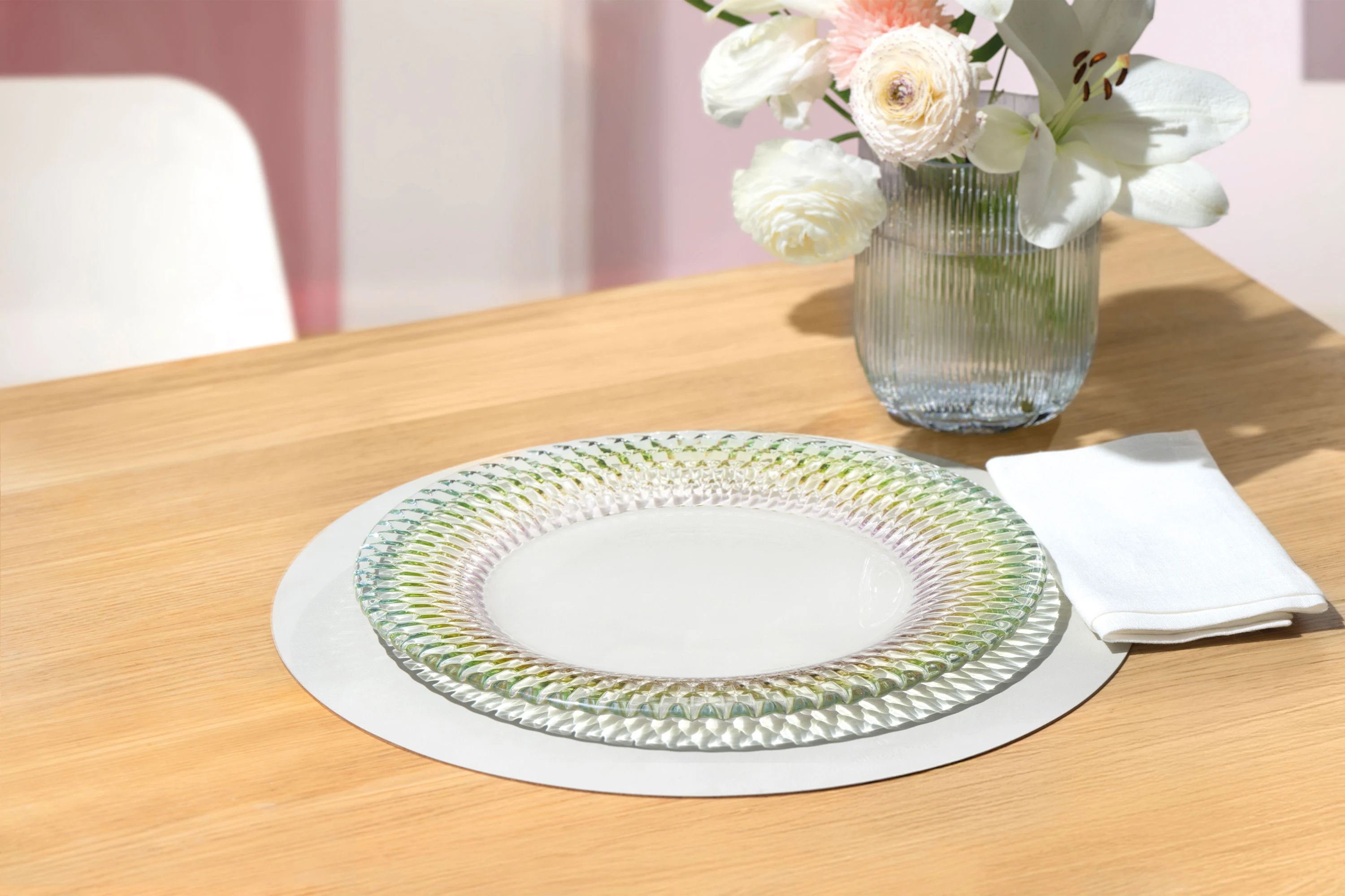 One Boston plate by Villeroy & Boch with a pink base are placed on a coaster next to a Fleur vase with white and pink flowers and a white napkin.