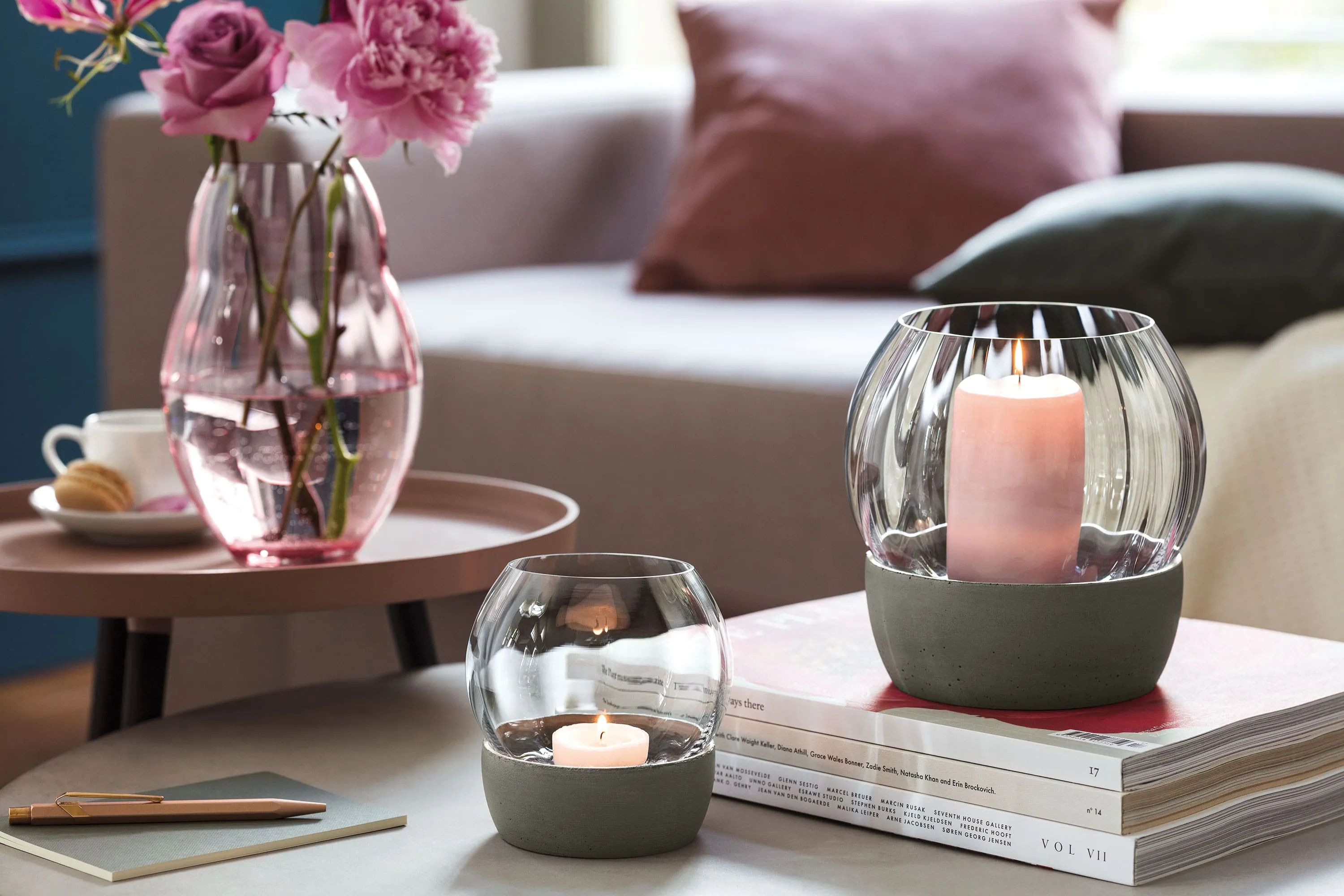 Two Rose Garden windglasses from Villeroy & Boch stand on a pile of books next to a pink Rose Garden vase with flowers, all on a round table in a cosy living room ambience.
