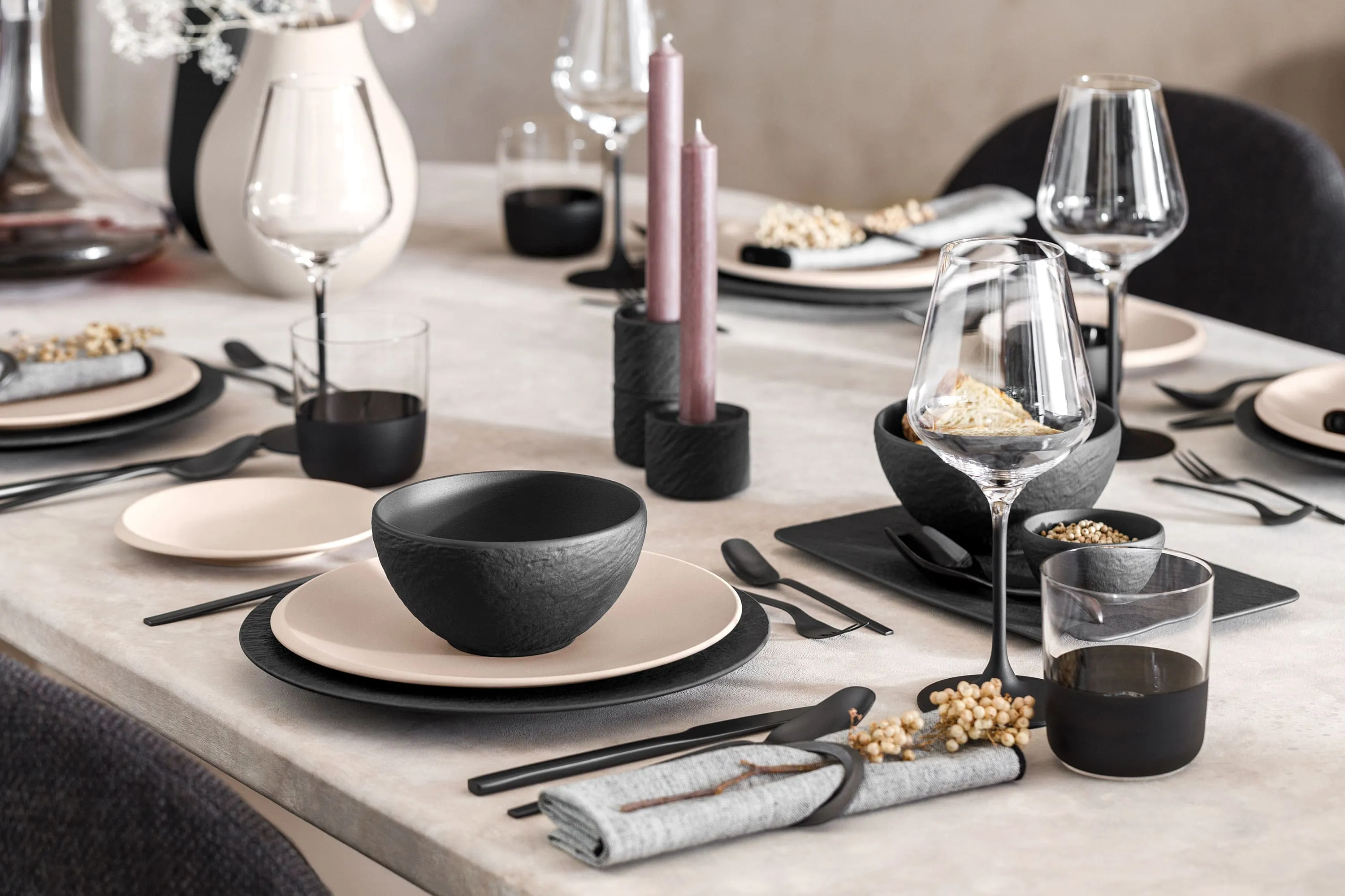 Des assiettes noires Manufacture et beiges NewMoon sur une table Une table dressée avec des assiettes Manufacture noires et NewMoon beiges ainsi que des couverts de table noirs.