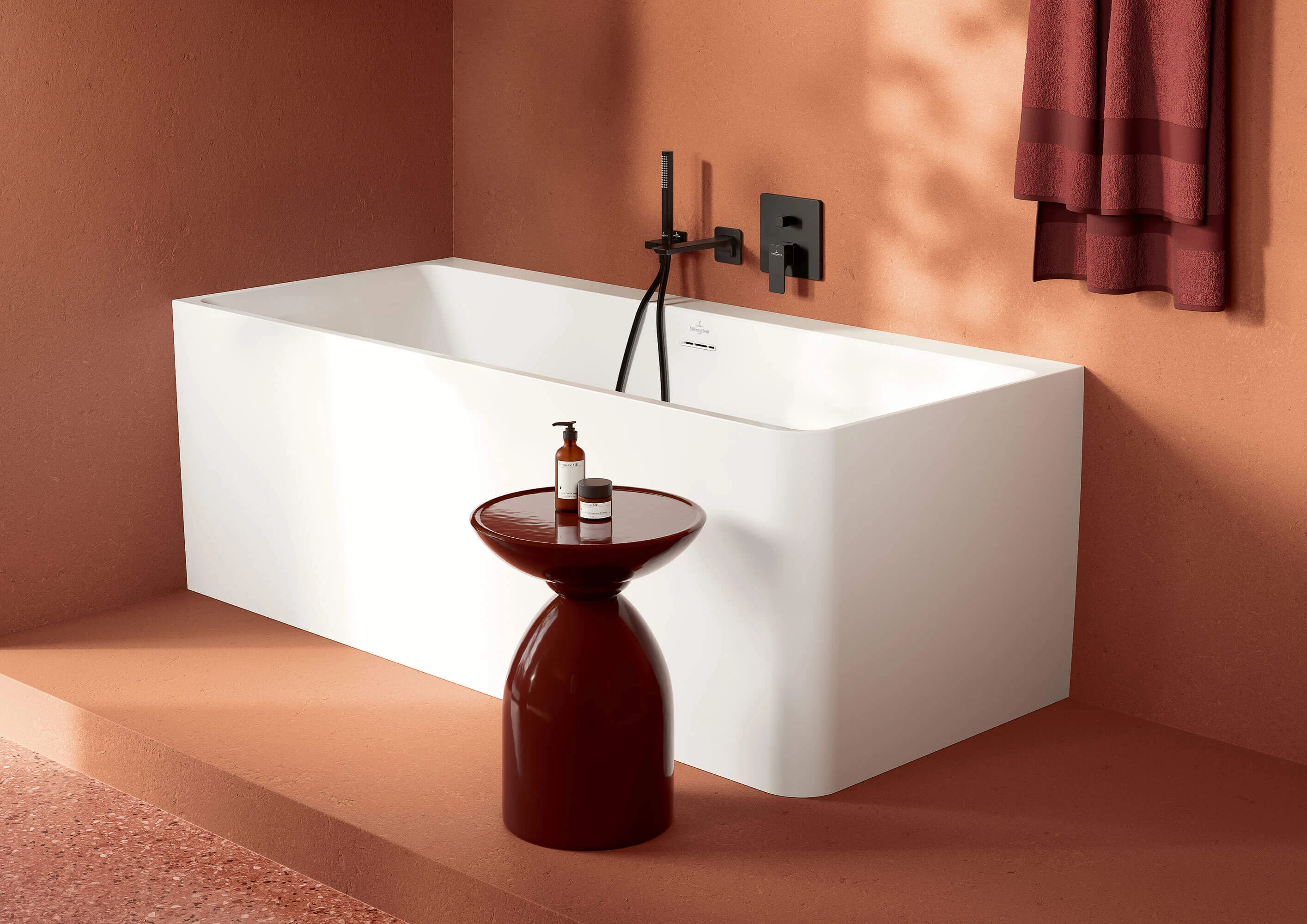 Hvit Subway 3.0 badekar med svarte armaturer Hvitt rektangulært badekar med svarte armaturer ved siden av et lite rundt brunt bord med en flaske på, foran en rød vegg.