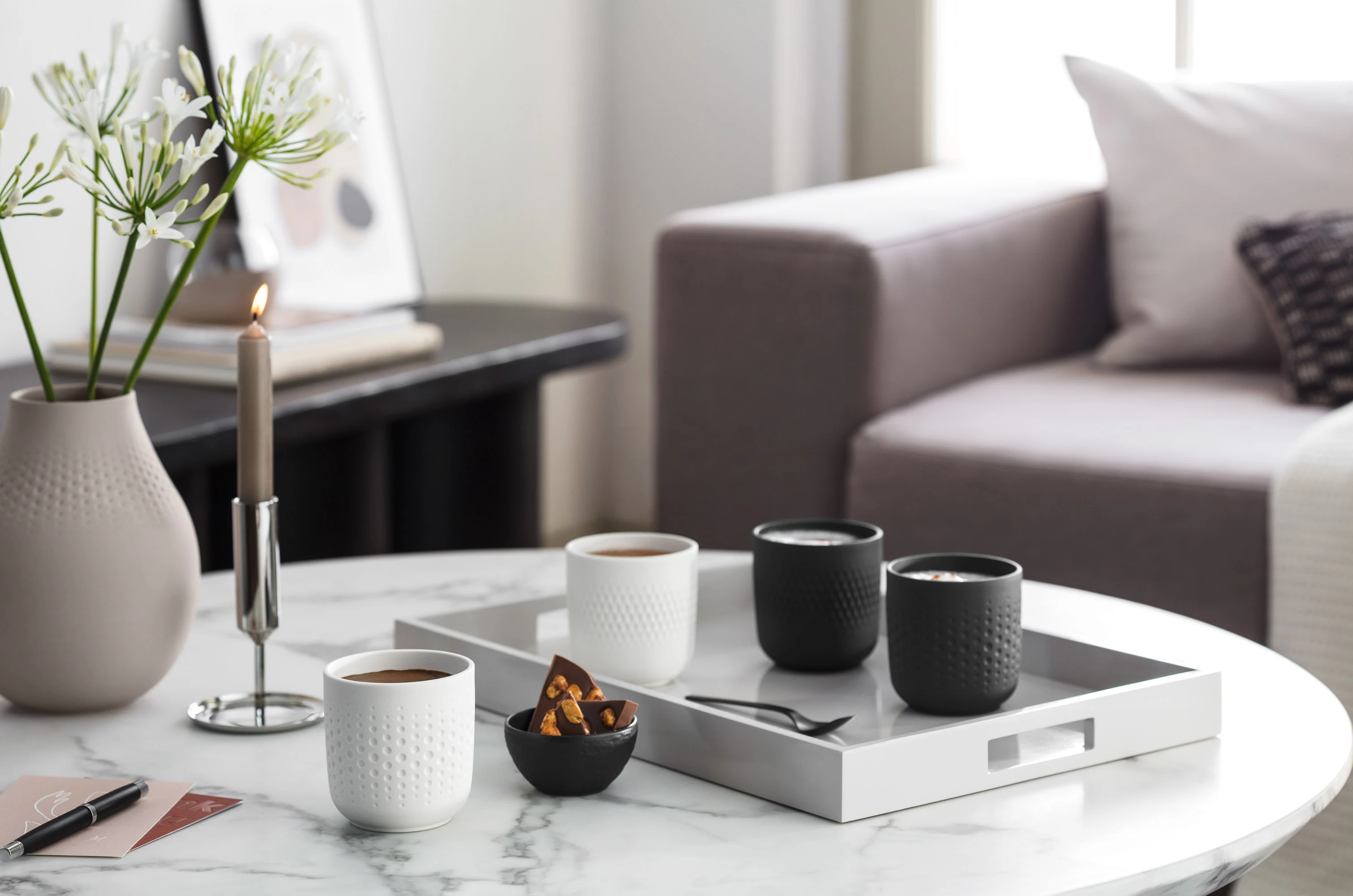 Elegant coffee table in a living room with Manufacture coffee mugs, candles, vases and a tray with cups and snacks.