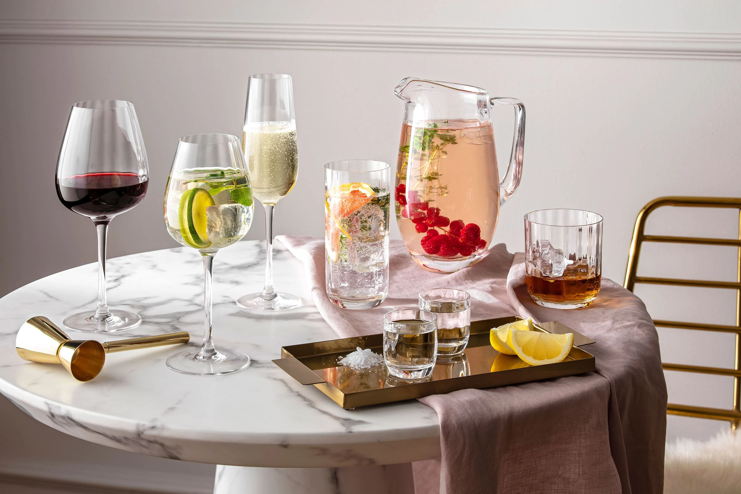 Glasses and jugs from the Villeroy & Boch Rose Garden collection on a round marble table with drinks and citrus fruits.