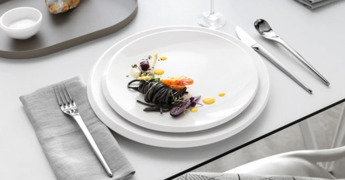 An elegant table setting with white plates and food from the NewMoon collection An elegant table setting with white plates and food from the NewMoon collection, beautifully arranged with cutlery.