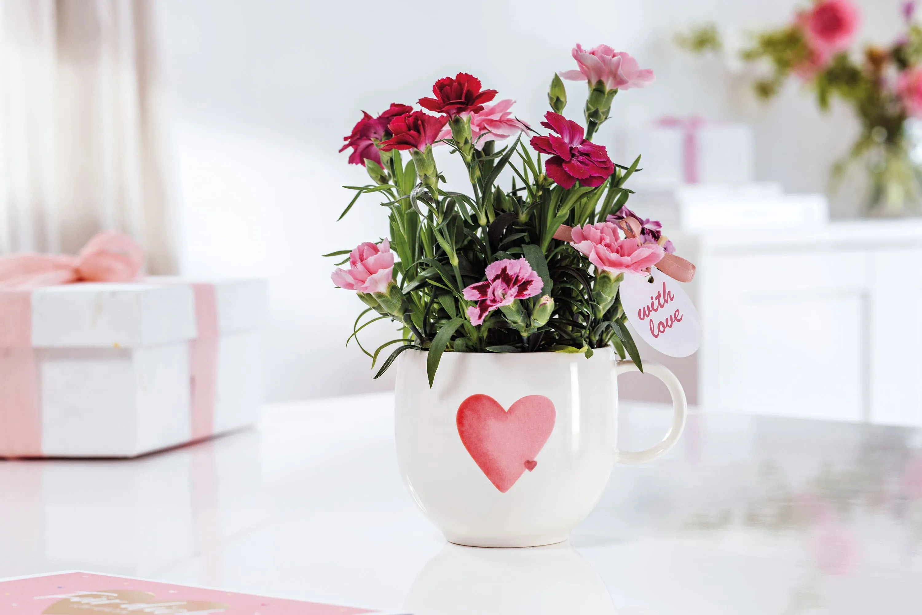 Une tasse blanche With Love avec un cœur rouge Une tasse With Love blanche avec un cœur rouge et des fleurs roses et rouges est posée sur une table blanche.