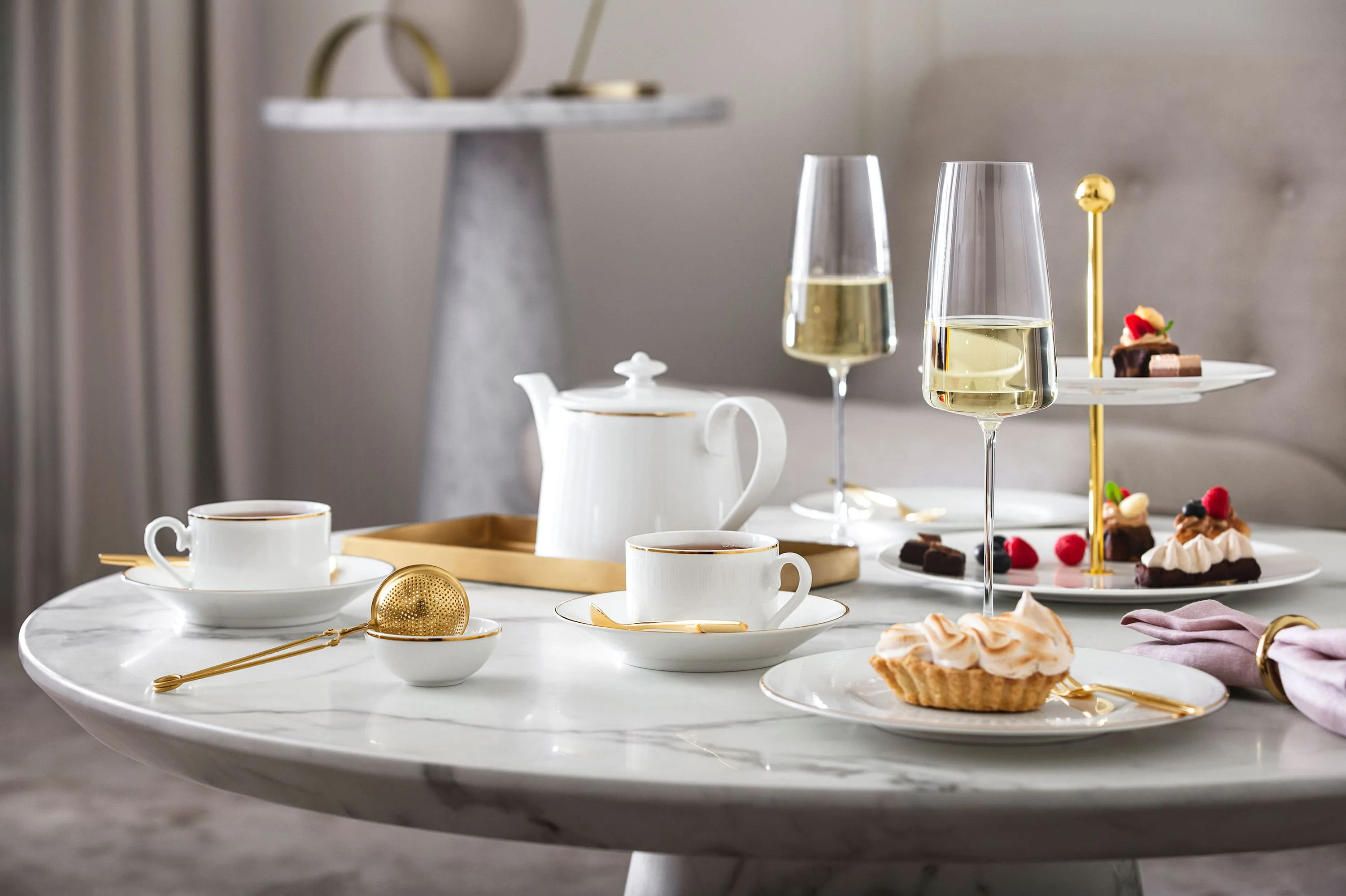 L’heure du thé à l’anglaise avec de la vaisselle Château Septfontaines et des verres MetroChic Une composition de table élégante pour le thé de l’après-midi avec des desserts et du champagne sur une table en marbre, servis sur de la vaisselle Château Septfontaines et avec des verres MetroChic.