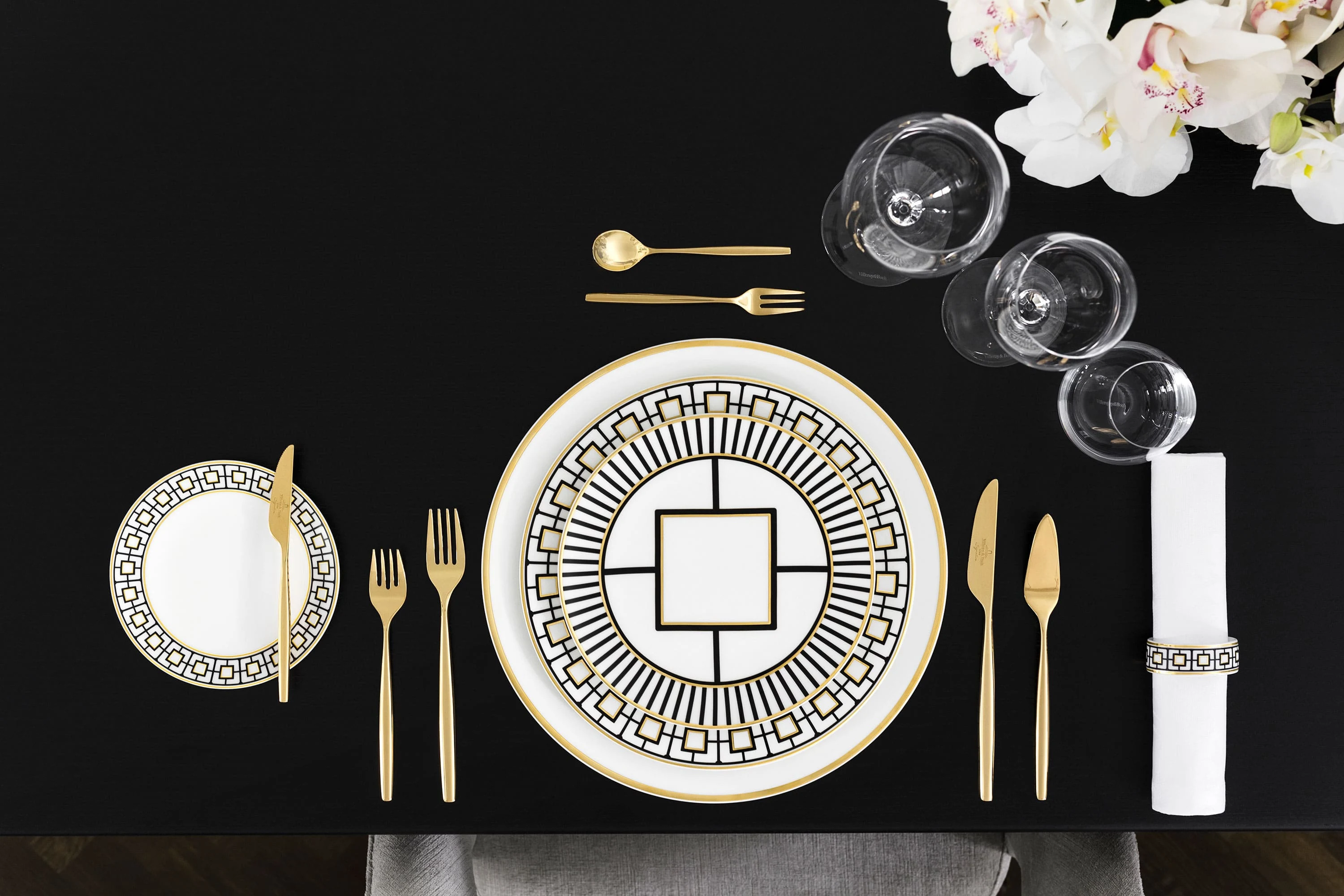 Elegant dining table decoration with gold-patterned MetroChic plates, gold cutlery and crystal glasses viewed from above.