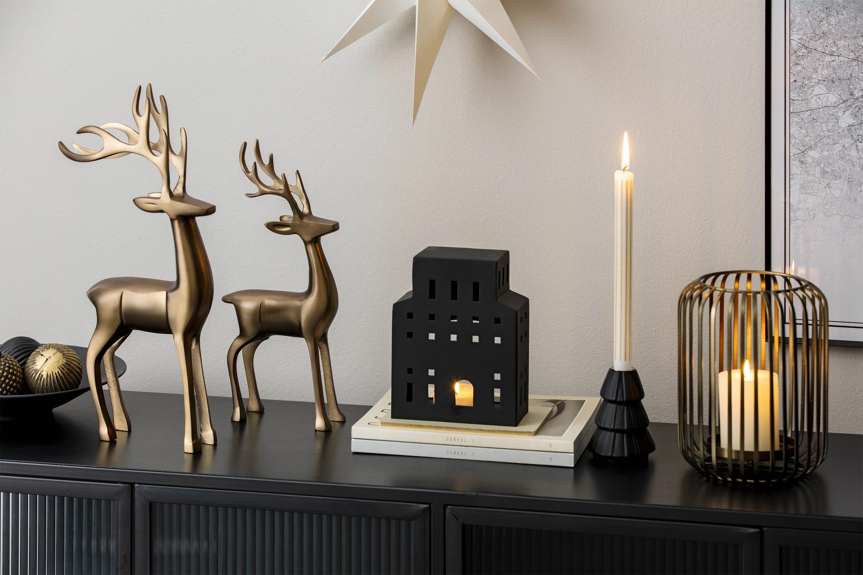 Two metal reindeer, candle holders and a black, house-shaped lantern on a black sideboard.