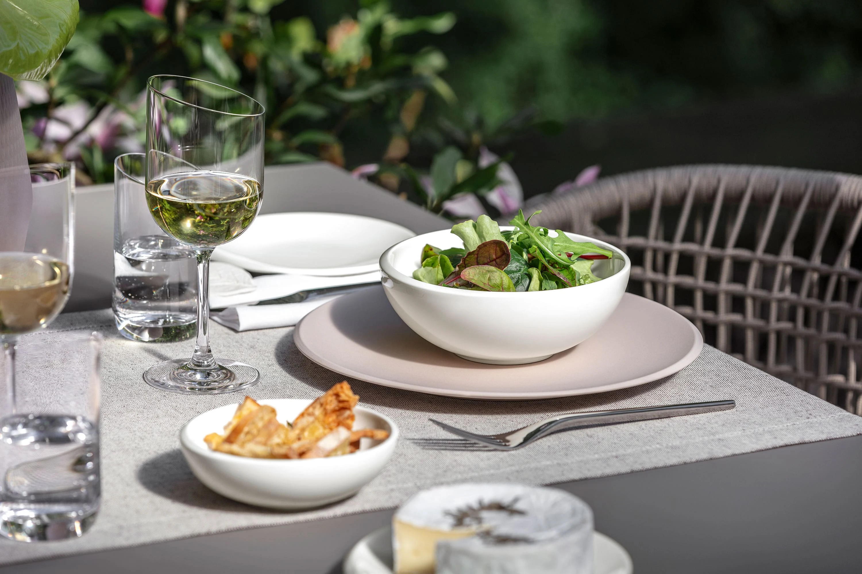 Weiße NewMoon Schüssel mit Salat auf beigem Speiseteller angerichtet Eine NewMoon Schüssel von Villeroy & Boch gefüllt mit Salat und Weingläsern.