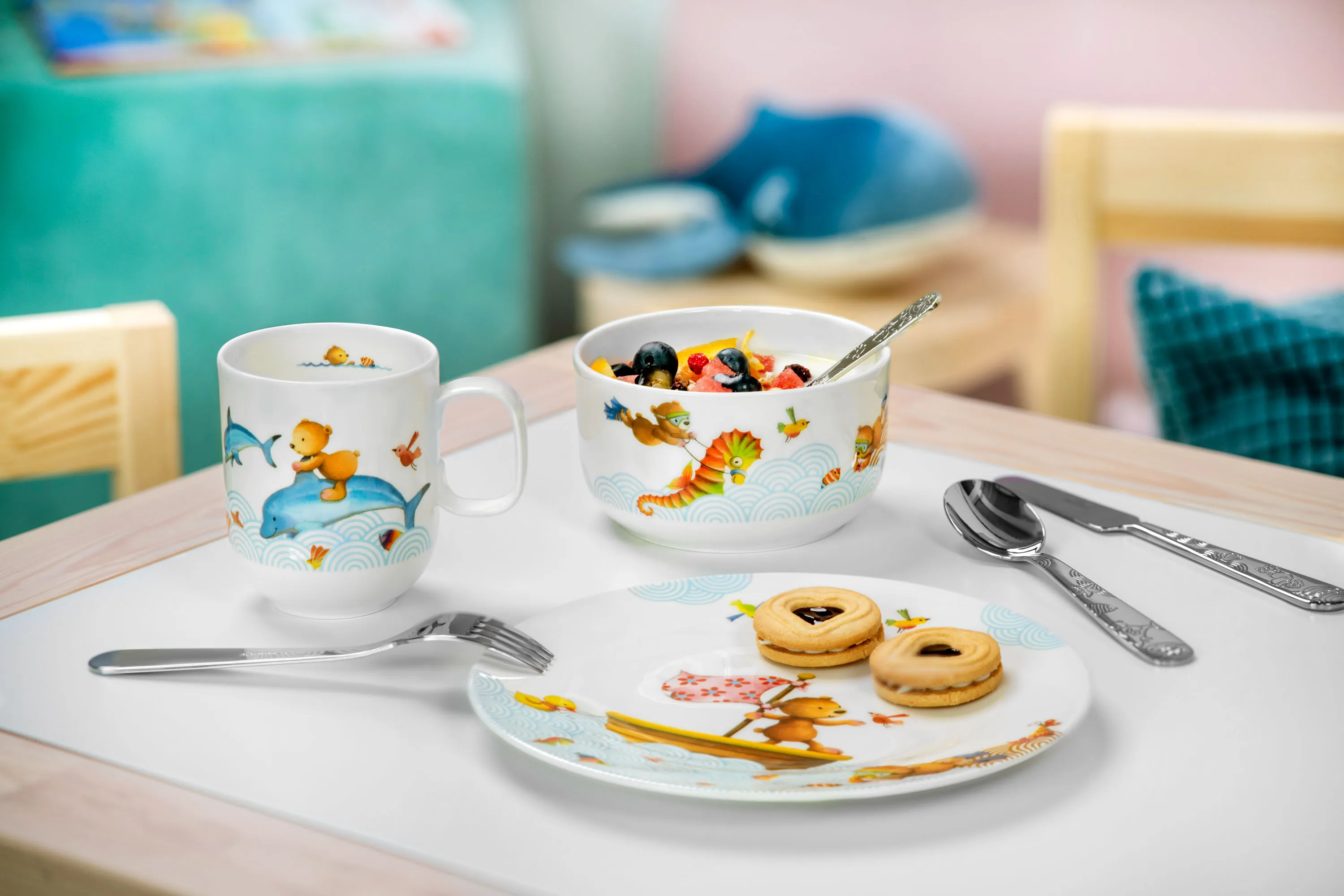 Breakfast setting with fruit salad, biscuits on a plate and two cups from the Happy as a Bear children's crockery series on a table.