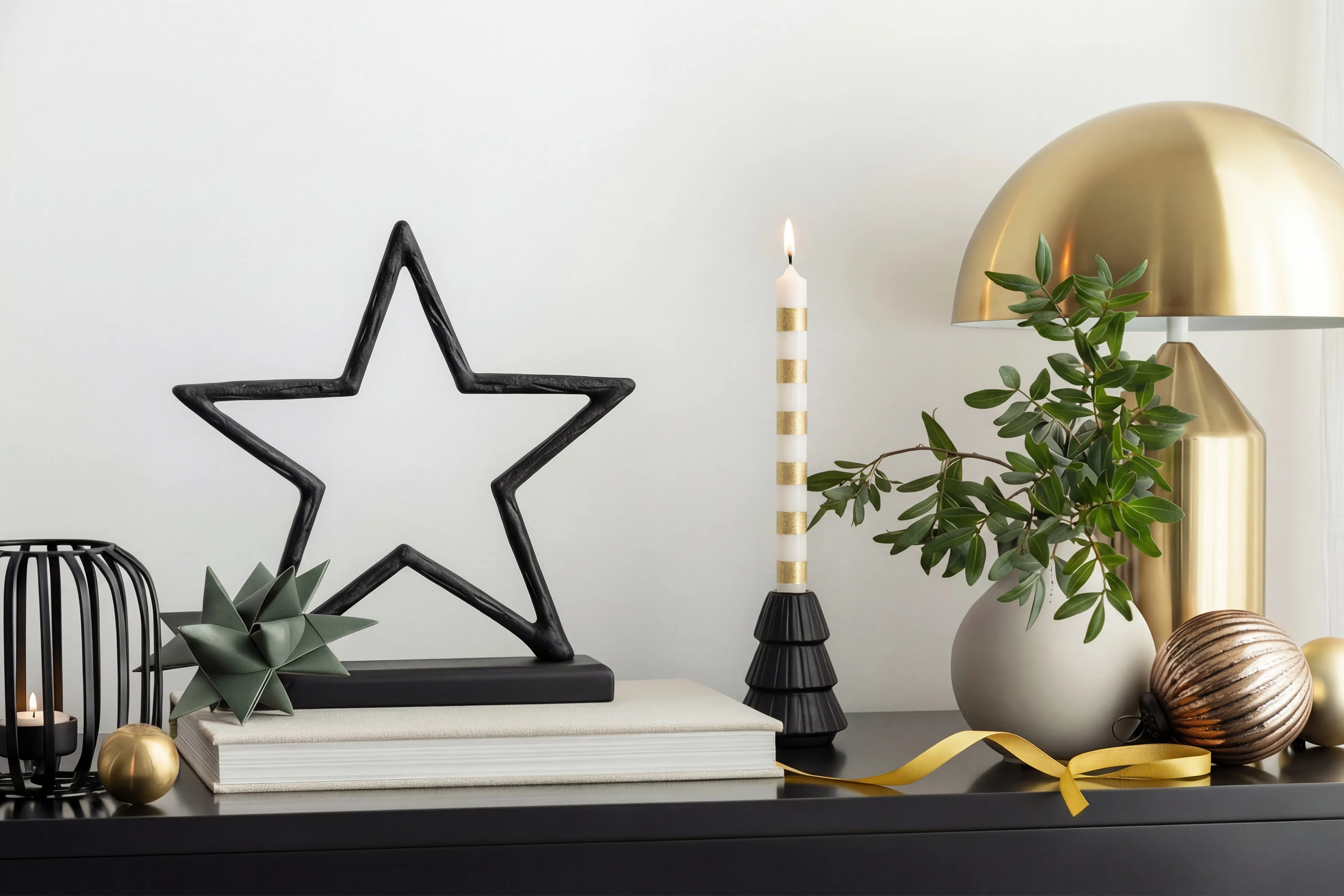 On a tabletop decorated with ornaments On a tabletop decorated with ornaments, there is a black star-shaped sculpture, a striped candle, a small plant and a golden lamp.
