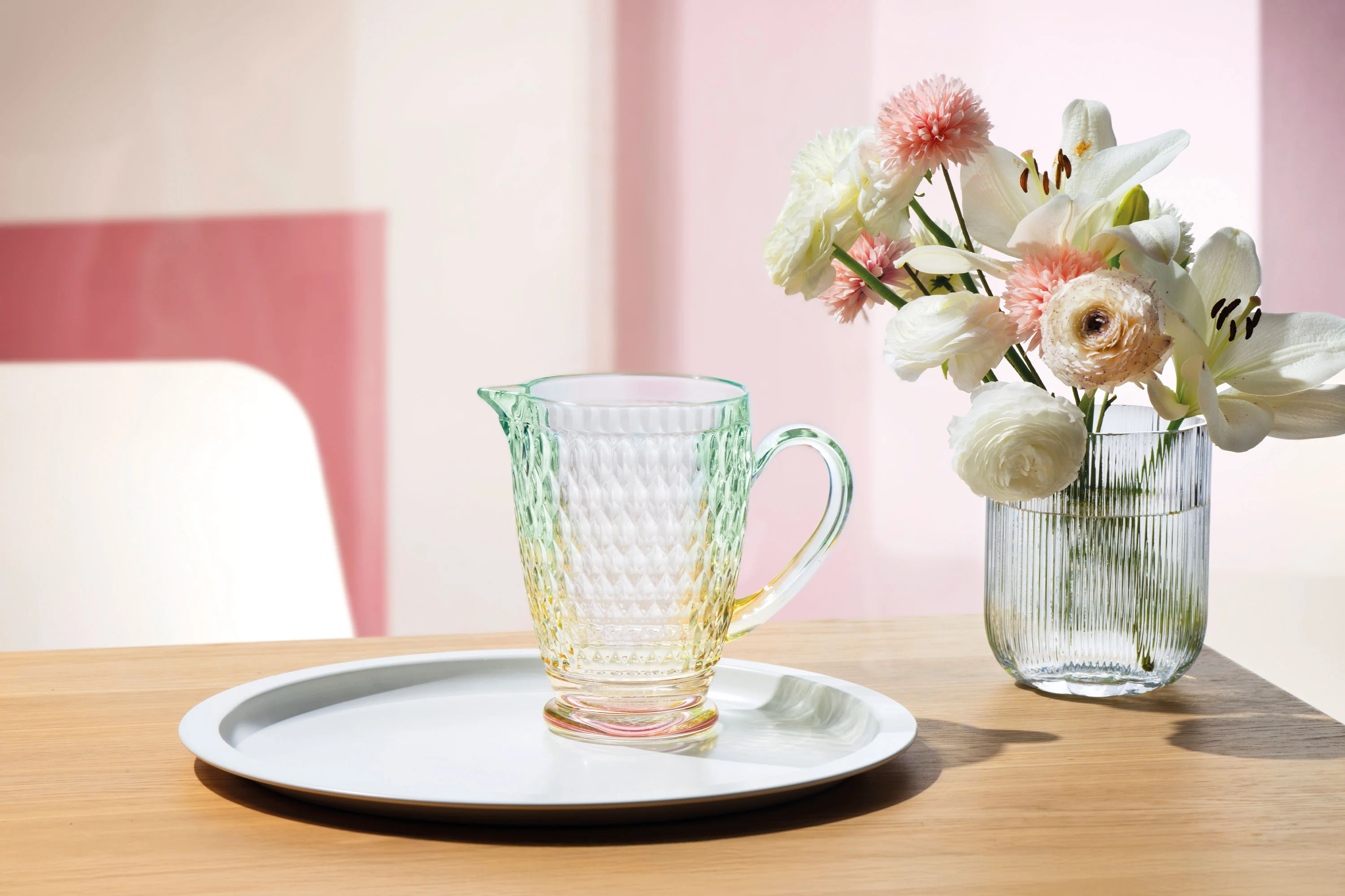 One Boston jug by Villeroy & Boch with a pink base are placed on a tray next to a Fleur vase with white and pink flowers.