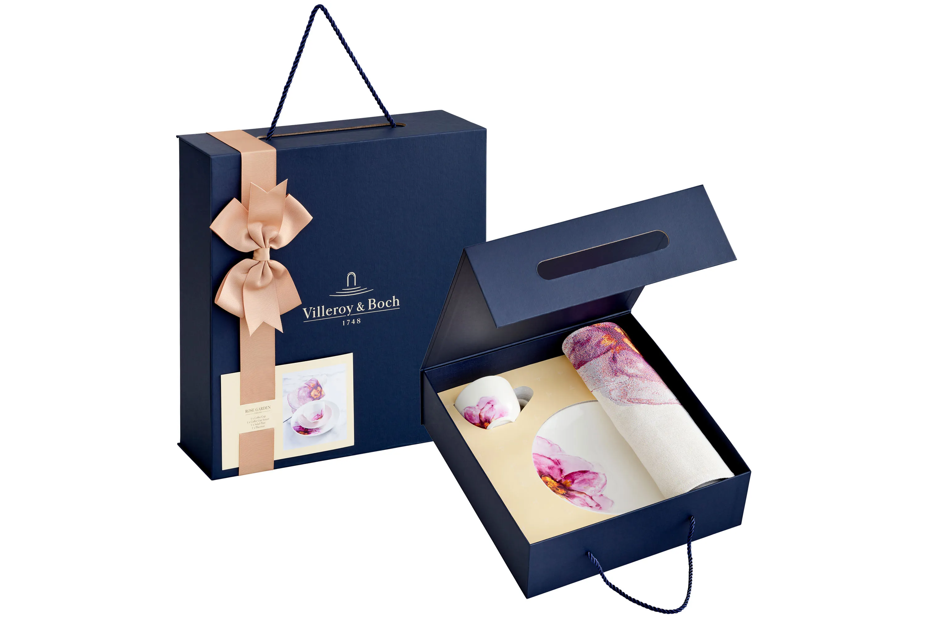 Rose Garden Gift Set Premium Villeroy & Boch Rose Garden Gift Box featuring floral themed tableware, presented in navy blue box with gold bow. Next to it, an open box showing the contents of the tableware with soft pastel tones and floral motif. Contains a coffee cup, pink saucer, salad plate and placemat securely nestled in the custom fit packaging.