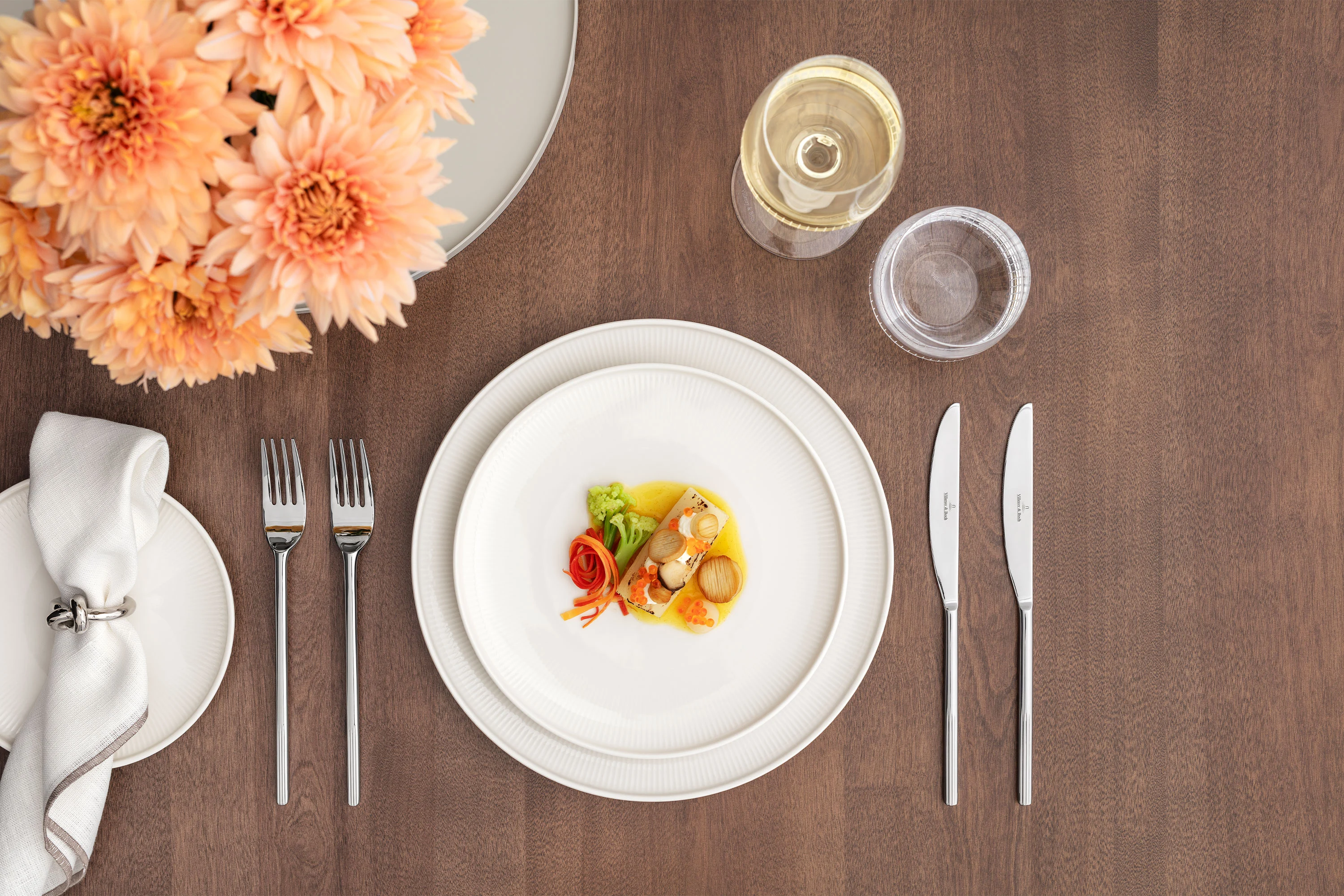 Une table formelle dressée avec la collection Afina, comprenant une petite assiette, un verre à vin, un verre à eau, des couverts, une serviette et un vase à fleurs.