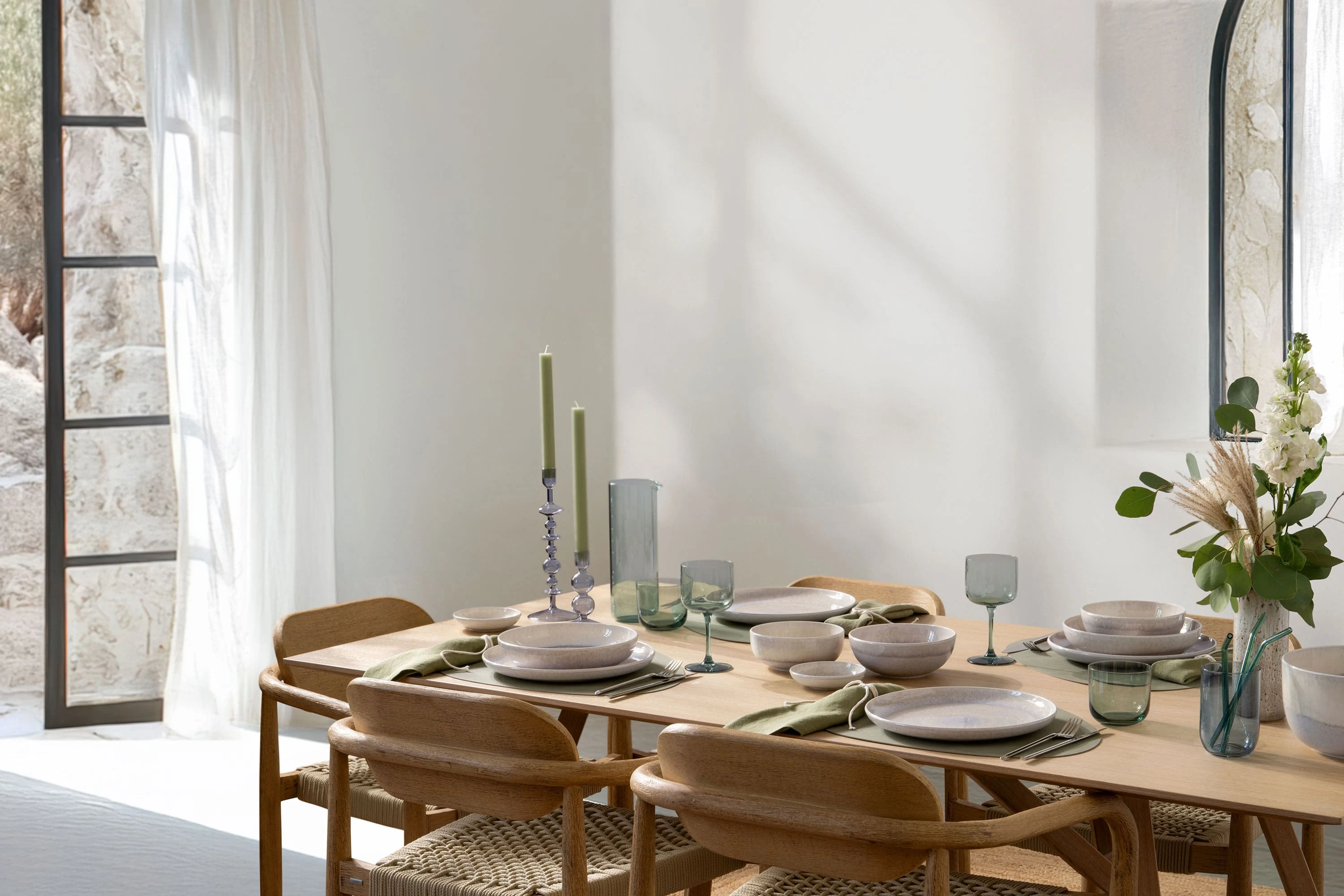 Tavola da pranzo moderna con bicchieri Villeroy & Boch Like Ice, porcellana Perlemor Sand, sedie in legno e decorazione naturale in una stanza luminosa con finestre aperte.