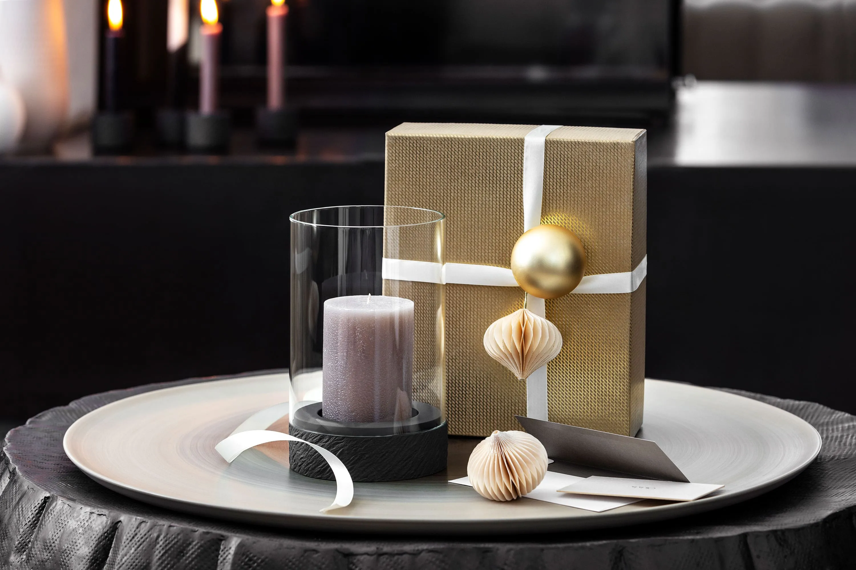 A Manufacture hurricane lamp with a candle A Manufacture hurricane lamp with a candle next to a gift wrapped with a white box and ornaments.