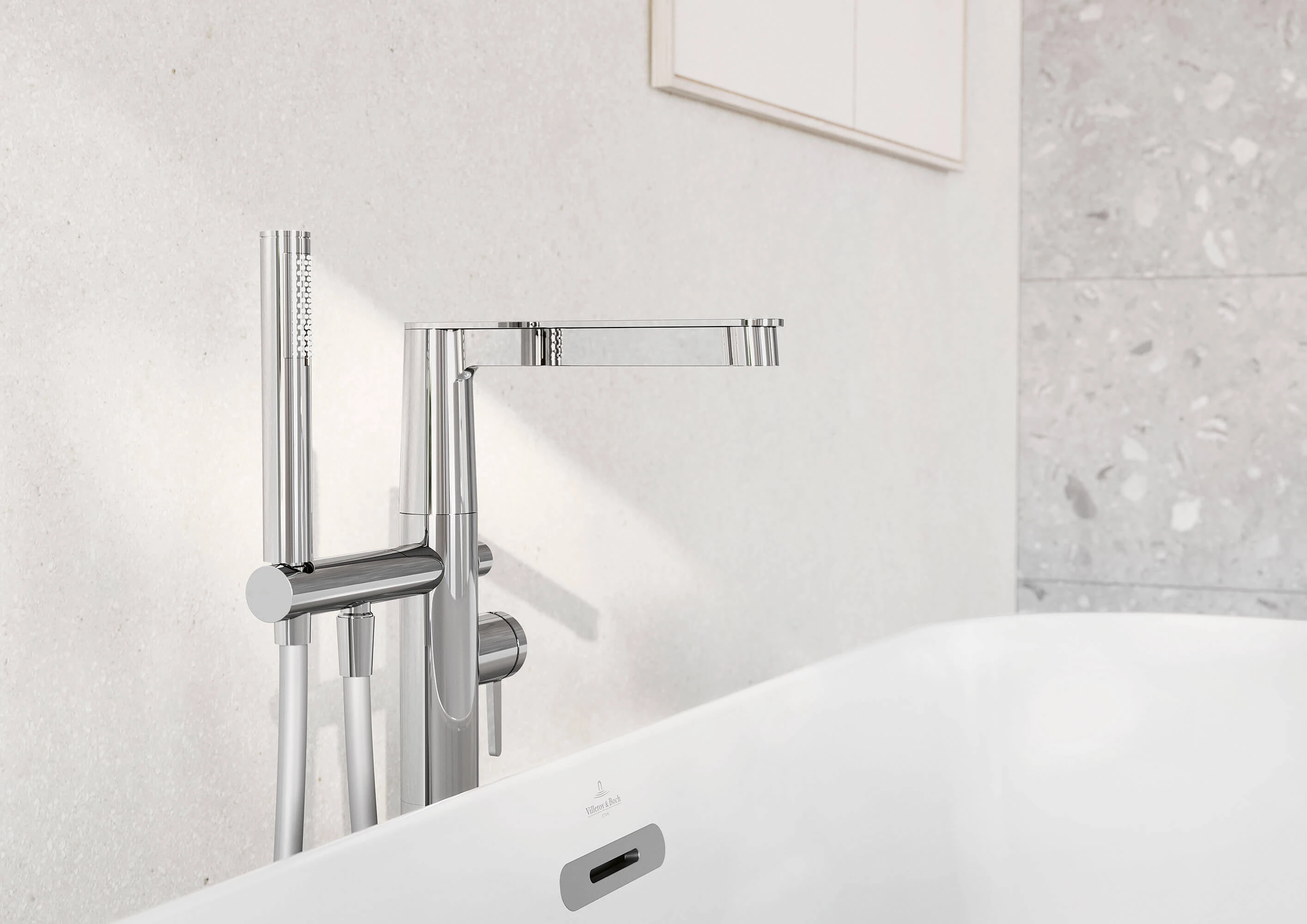 Conum-badekararmatur med hånddusj Foran en hvit, flislagt vegg er det montert en moderne, forkrommet badekararmatur med hånddusj. Det hvite badekaret er delvis synlig i forgrunnen.