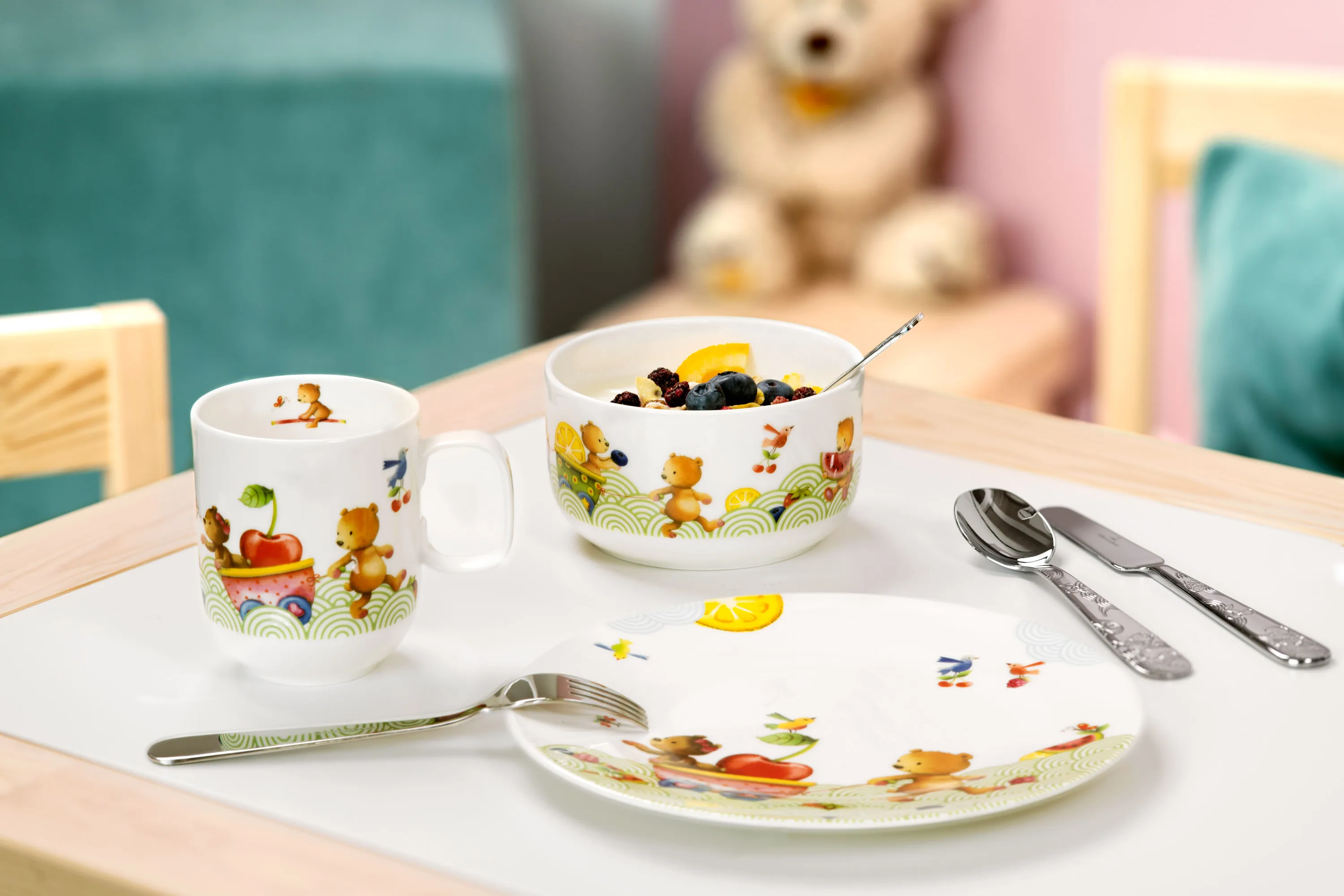 A Hungry as a Bear breakfast set with a bowl of muesli and fruit on a table, along with a cup, cutlery and a teddy bear in the background.