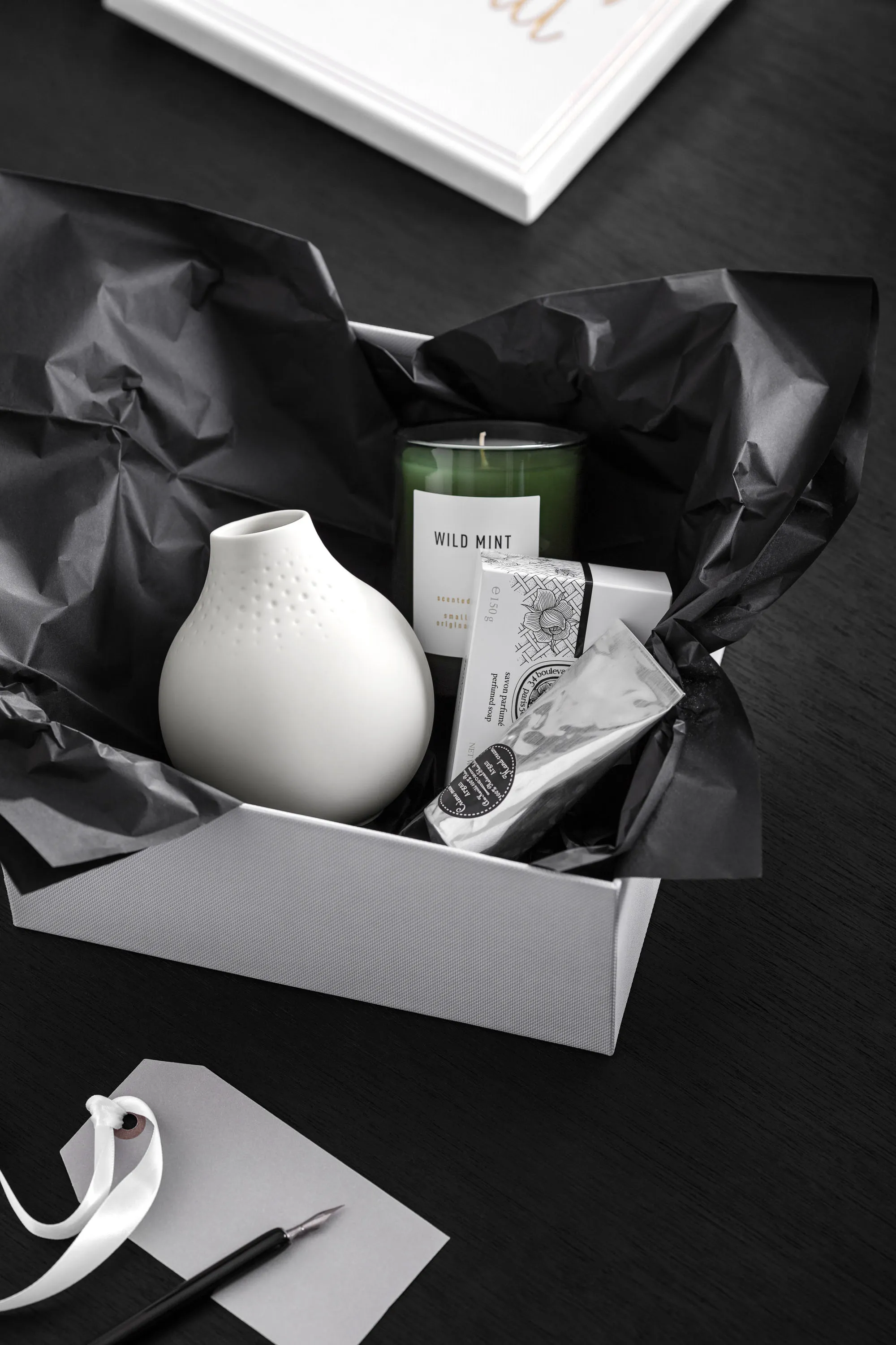 Un petit vase Manufacture blanc dans un emballage cadeau Une boîte contenant un petit vase Manufacture blanc de Villeroy & Boch avec un tube de crème et une bougie dans un verre.