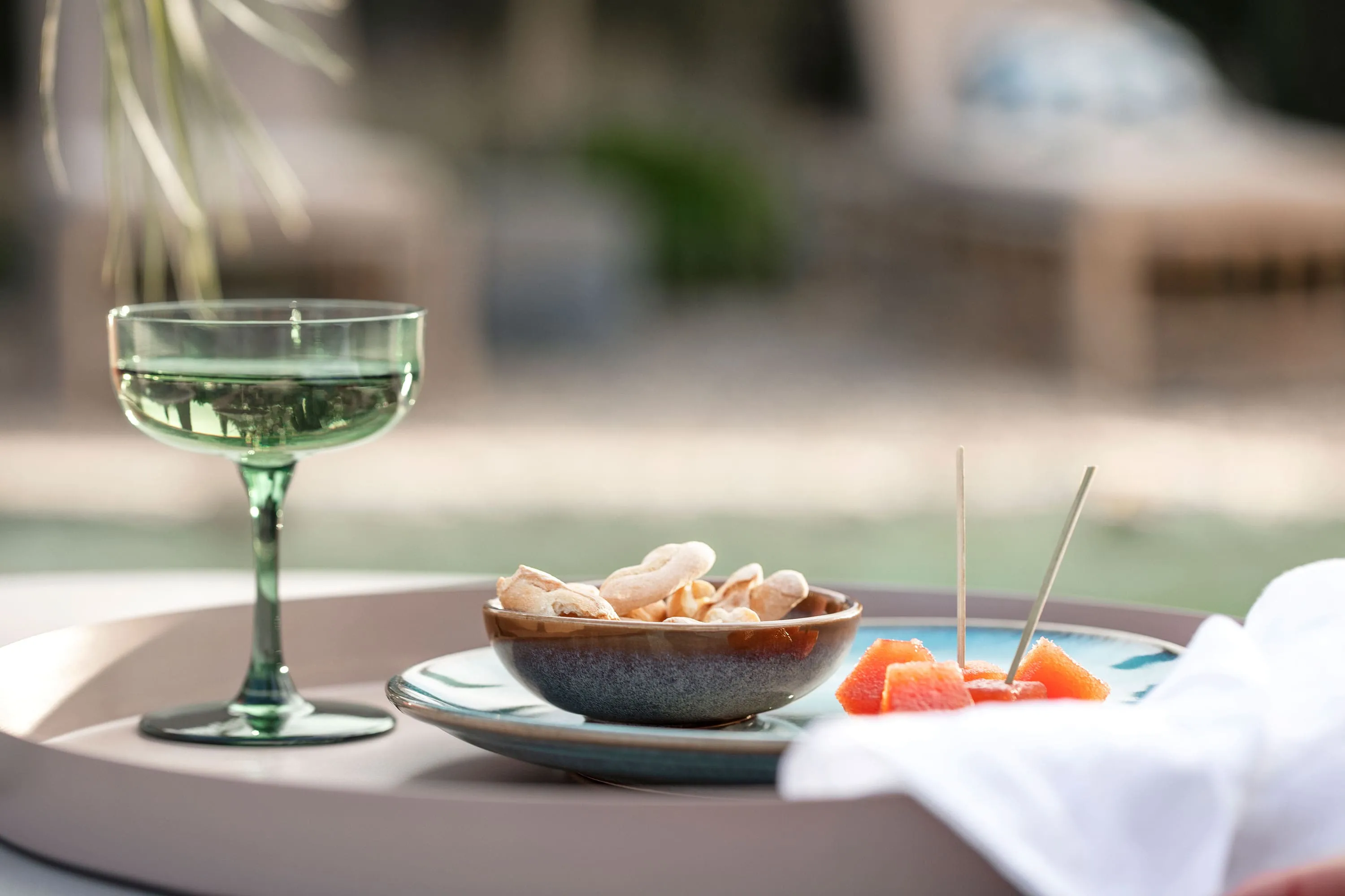 A Like Sage glass, a Lave bowl of crackers and slices of orange on a tray outdoors.