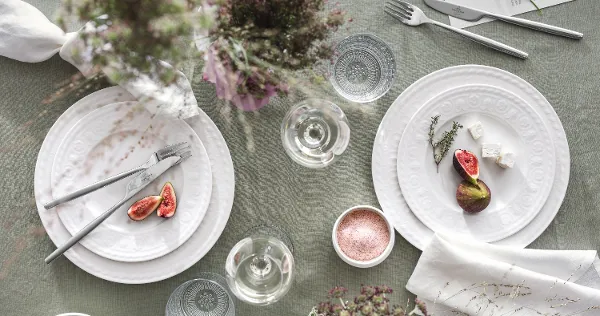 Villeroy & Boch Cellini plates with figs, cheese and herbs on a beautifully laid table. Glasses, cutlery, delicate flower arrangements and a bowl of salt on a green tablecloth add the finishing touches to the ambience.