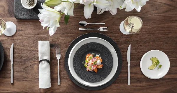 Décoration de table élégante avec un plat de fruits de mer sur des assiettes Manufacture, des fleurs blanches, un verre de vin blanc et une petite assiette avec des tranches de citron.