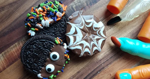Three Halloween cookies: two with googly eyes and sprinkles, one with a white spider web pattern on a wooden surface. Read More 